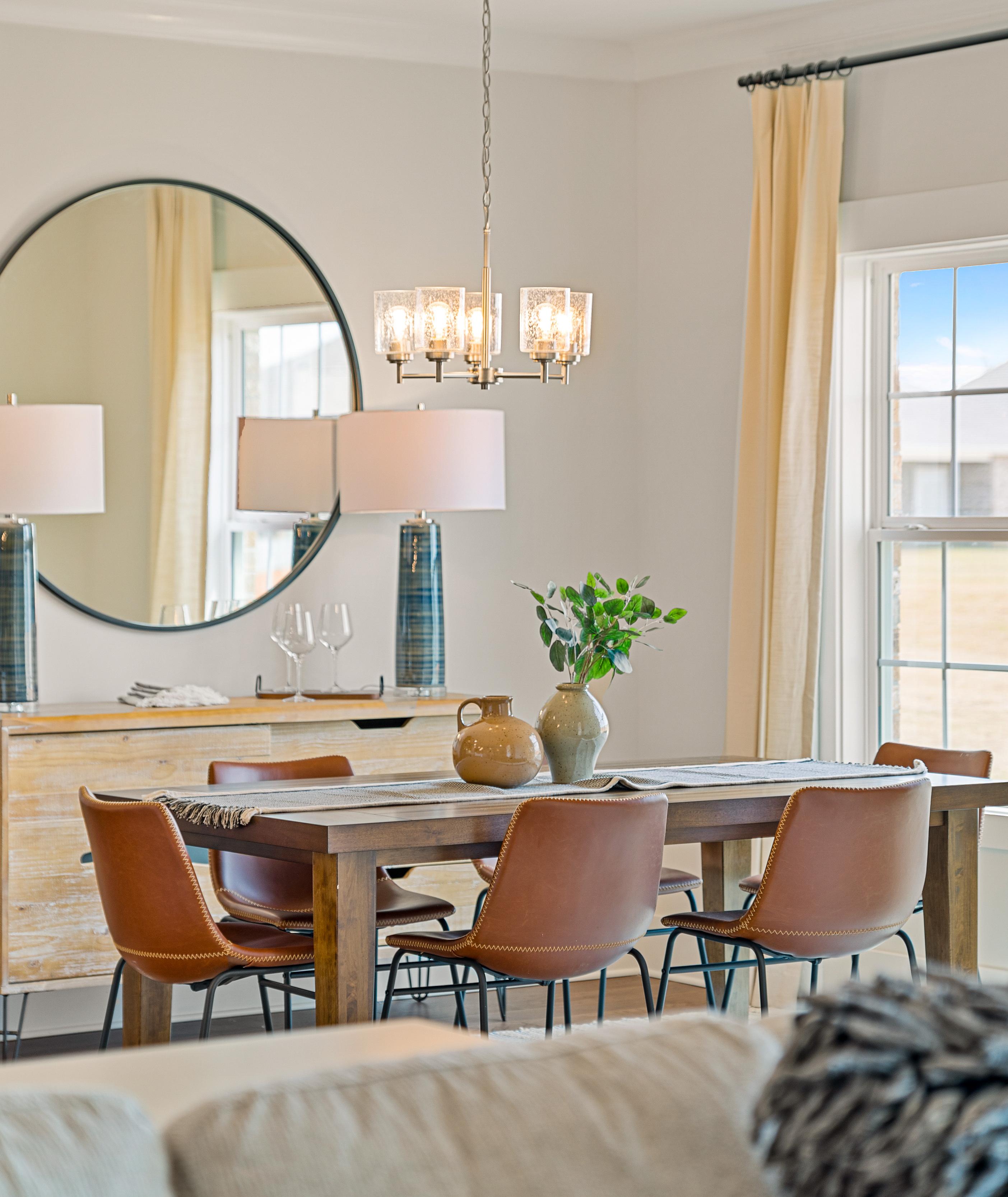 Elegant dining room in Pikes Ridge home, Meridianville Alabama with wooden table, leather chairs, round mirror, and chandelier by Davidson Homes