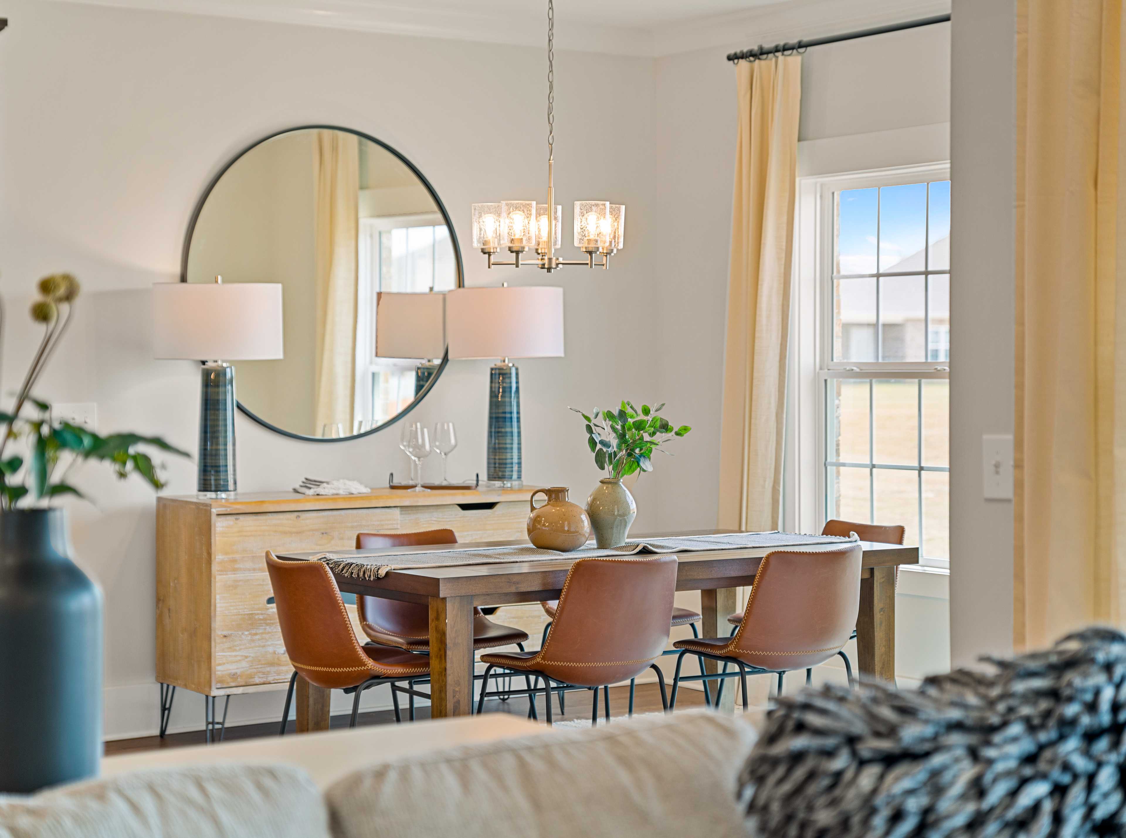 Elegant dining room in Pikes Ridge home, Meridianville Alabama with wooden table, leather chairs, round mirror, and chandelier by Davidson Homes