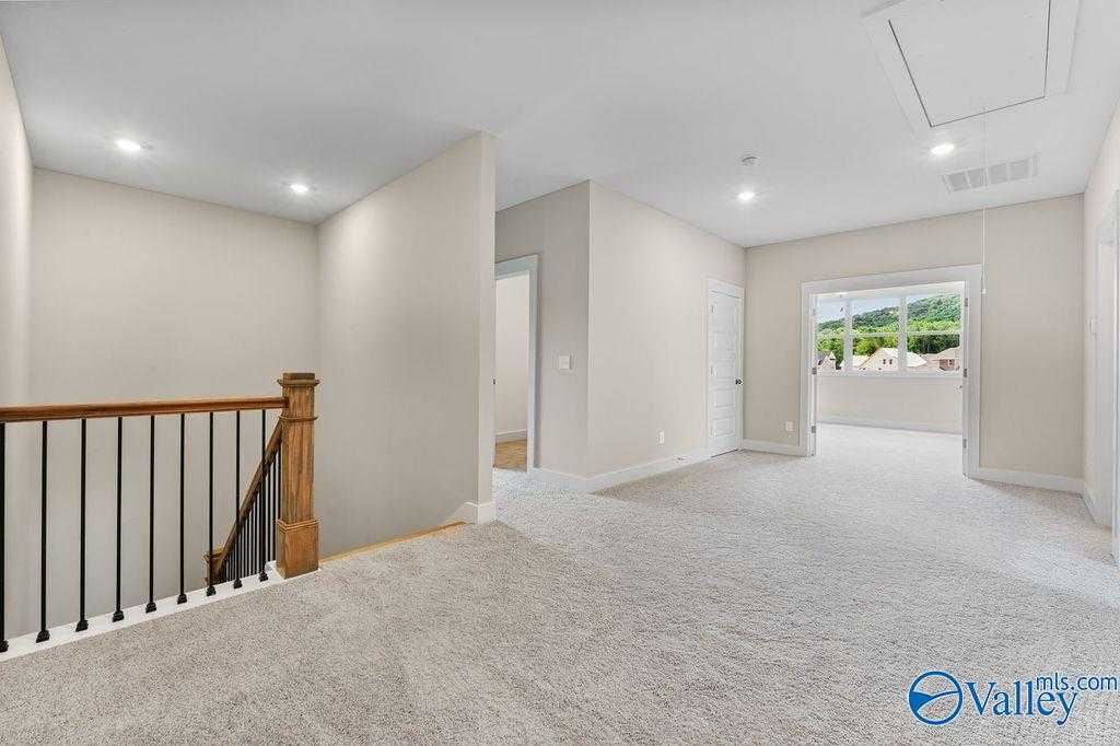 Bright upstairs hallway with wooden staircase, beige walls, carpeted floor, and valley-view window in The Oxford 5-bedroom home, Owens Cross Roads, AL