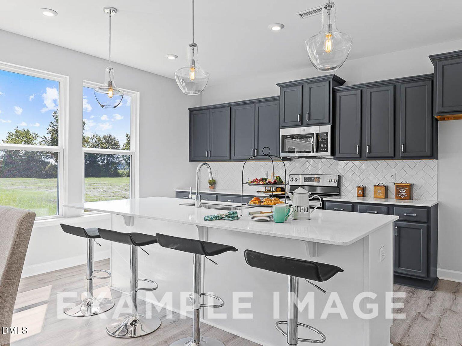 Modern kitchen with white quartz island, gray cabinets, stainless appliances, subway tile backsplash, and large windows in The Chestnut B by Davidson Homes, Lillington, NC