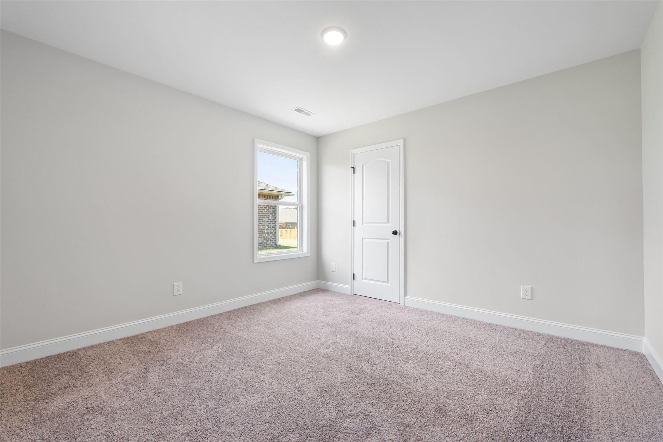 Bright, carpeted bedroom with neutral walls in The Holly C floor plan by Davidson Homes in Anna, Texas.