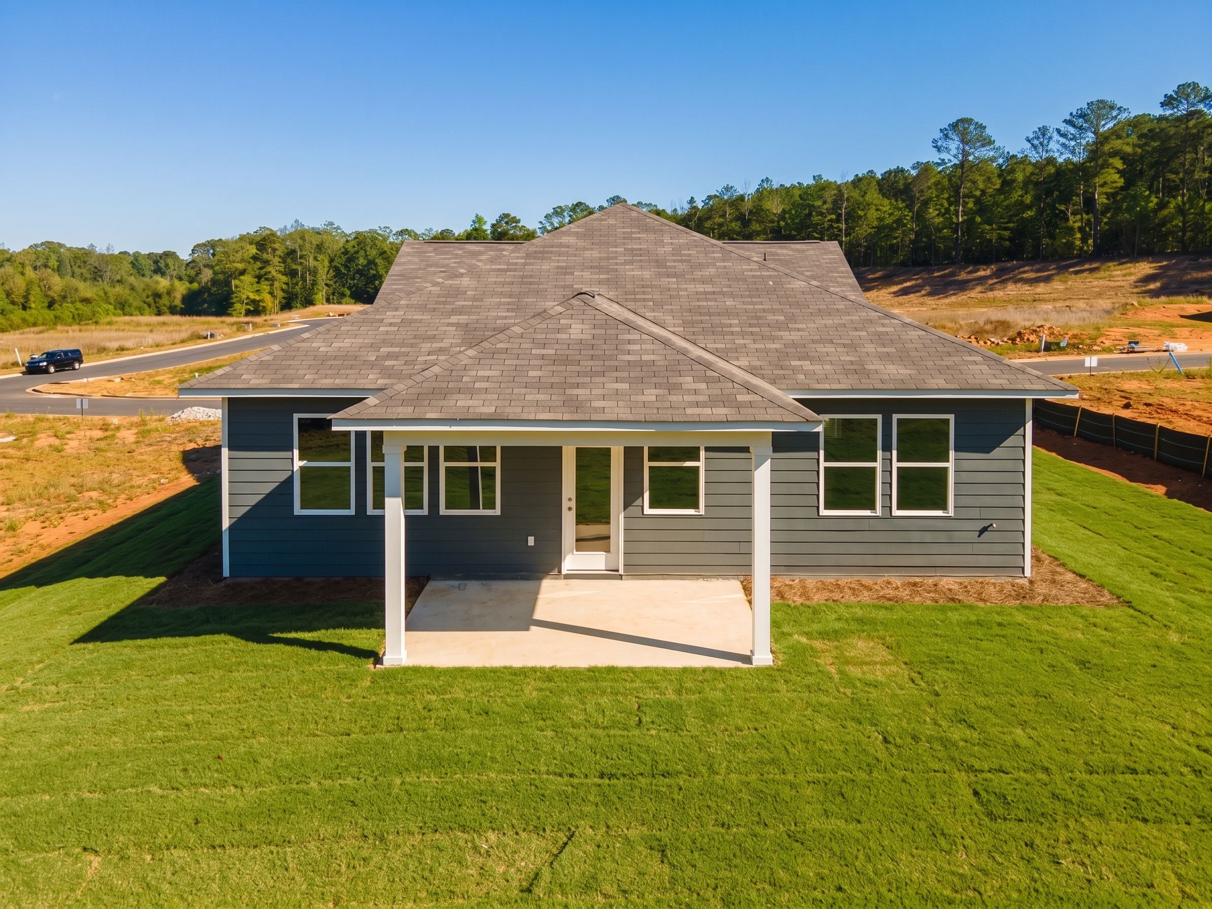 Rear view of gray single-story The Luna B home by Davidson Homes, covered patio, large windows, wooded lot in Anderson Lakes, Opelika, Alabama