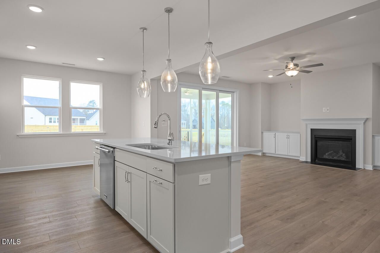 Modern open-concept kitchen with white island, pendant lights, and adjacent living room fireplace in Davidson Homes The Cypress D II, Angier, NC