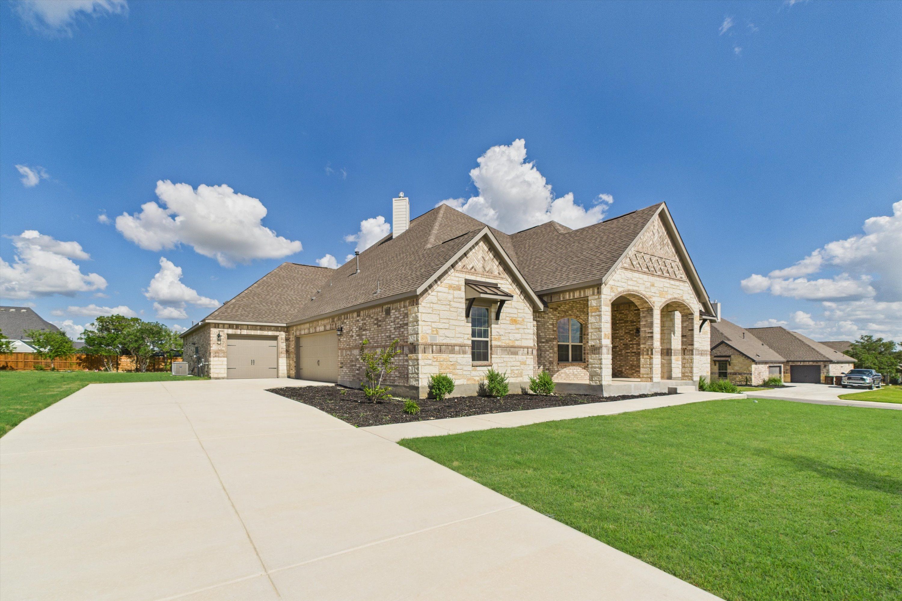 Stone brick 1-story home with gabled roof, 3-car garage, and landscaped yard in Potranco Oaks, Castroville, Texas