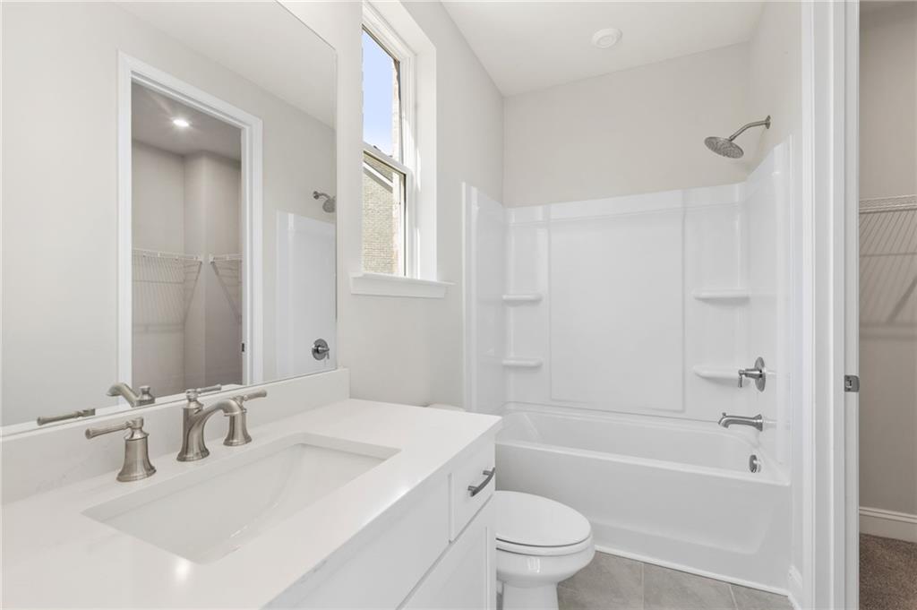 Modern secondary bathroom with dual sinks, soaking tub, glass shower, and walk-in closet in The Danbury C, Buford, Georgia