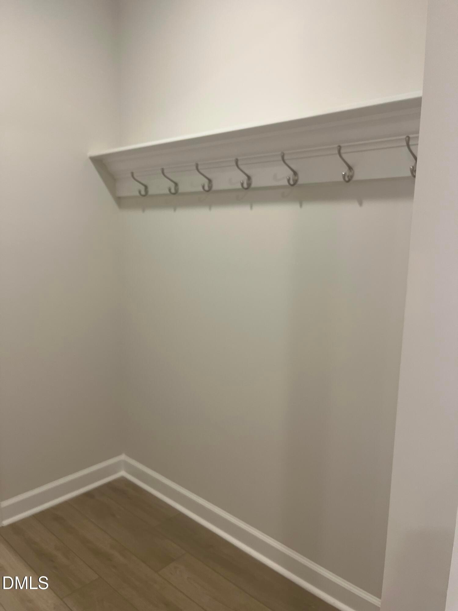White wooden shelf with metal hooks in organized entry closet, hardwood floors in Davidson Homes Ashport G, Wake Forest NC