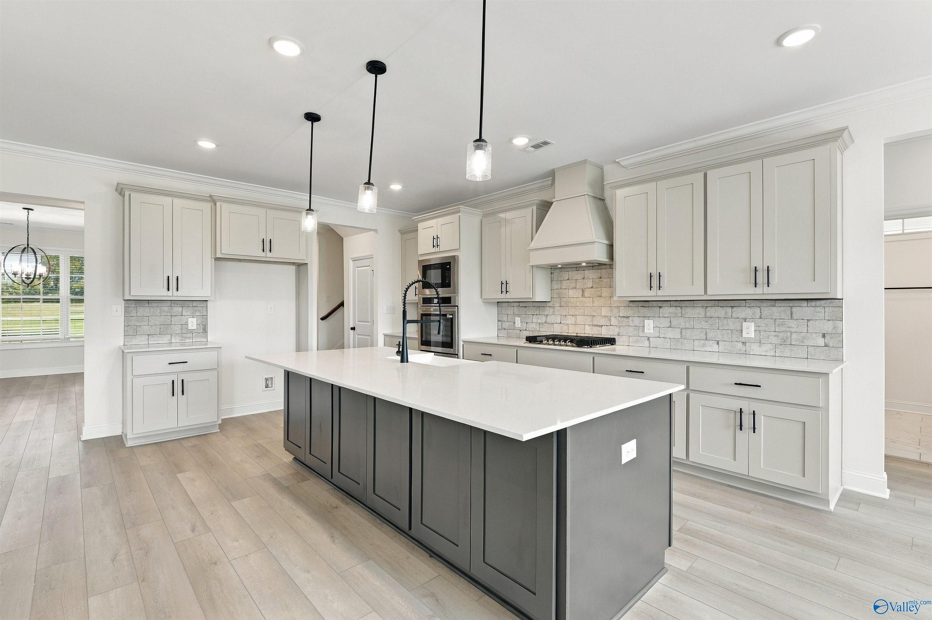 Modern kitchen with gray island, white quartz countertops, subway tile backsplash, and pendant lights in Davidson Homes Huntsville home