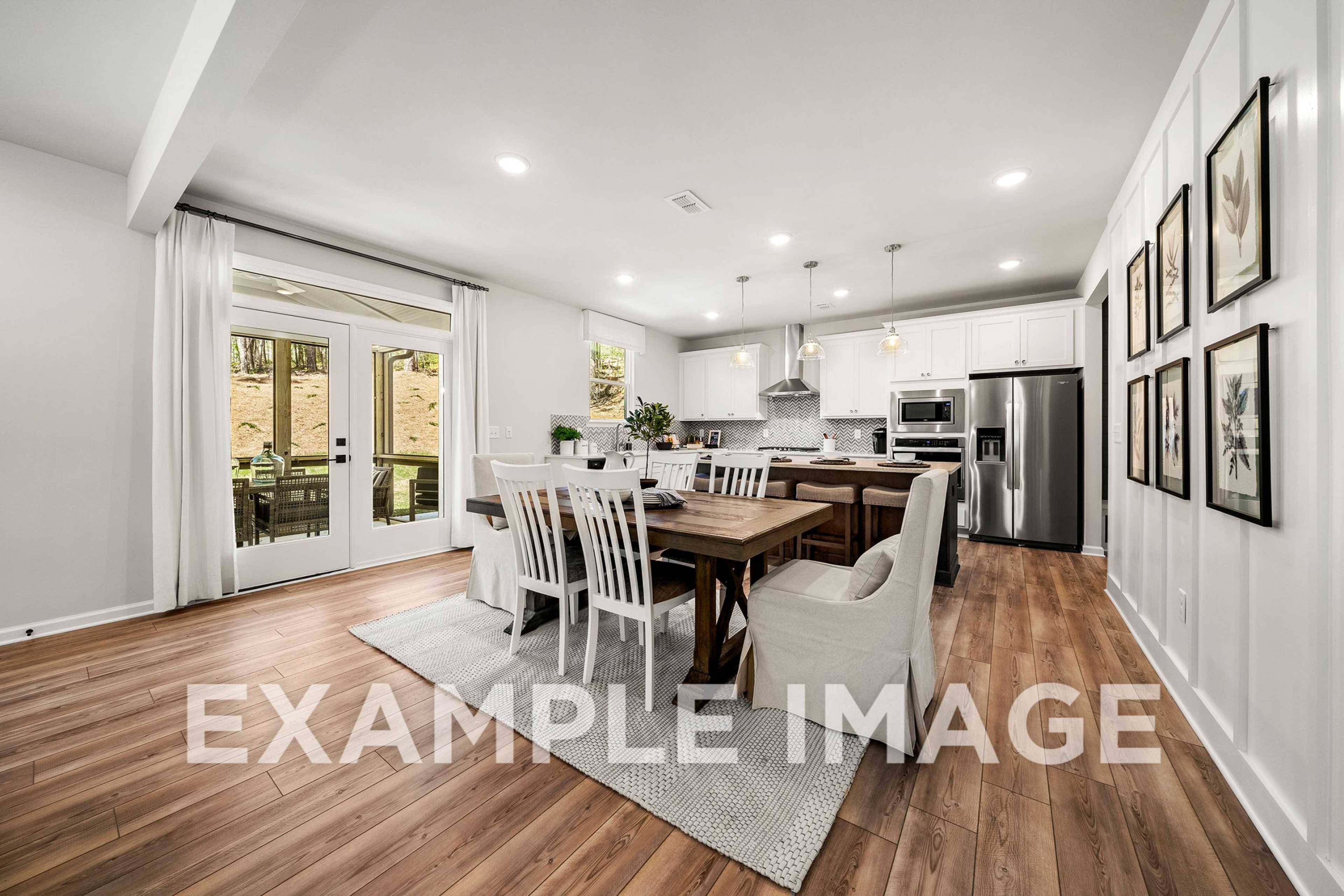 Spacious open-concept kitchen and dining in The Hickory A featuring white cabinets, stainless appliances, farmhouse table, and French doors to patio