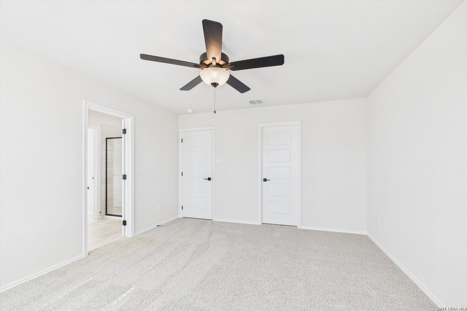 Bright bedroom with white walls, carpet floor, ceiling fan, en-suite bath, and closet doors in Davidson Homes The Gillian B, San Antonio