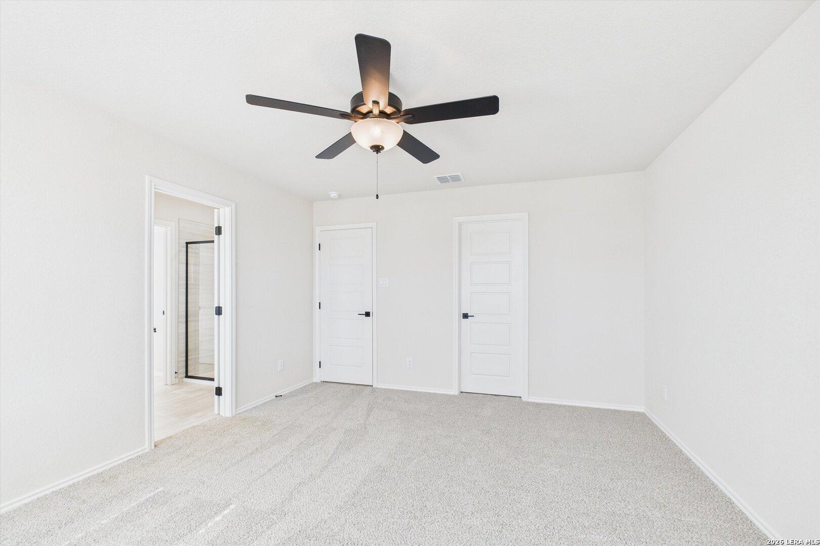 Bright bedroom with white walls, carpet floor, ceiling fan, en-suite bath, and closet doors in Davidson Homes The Gillian B, San Antonio