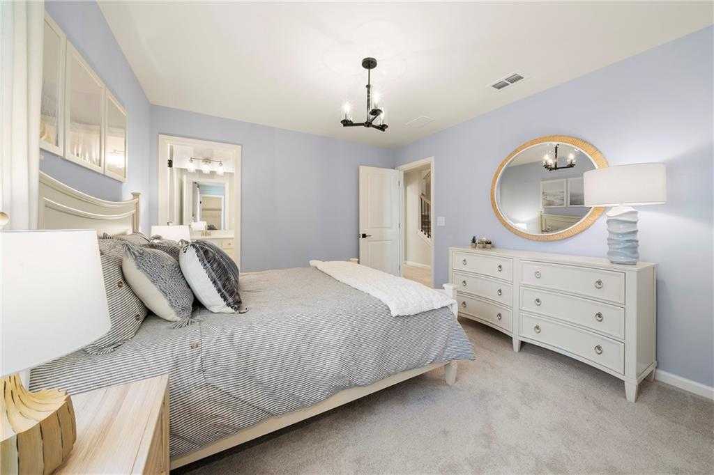 Cozy blue-walled bedroom with king bed, mirrored dresser, and chandelier in Davidson Homes The Hickory B, Riverwood, Dallas, GA