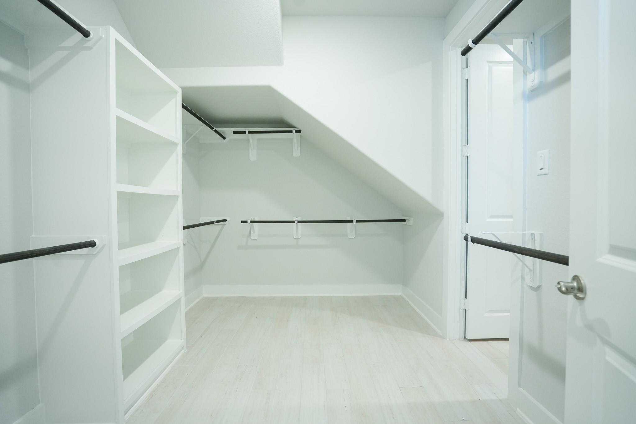 Spacious walk-in closet with white built-in shelving, hanging rods, and light wood flooring in Davidson Homes The Edward C, Lago Mar, Texas City