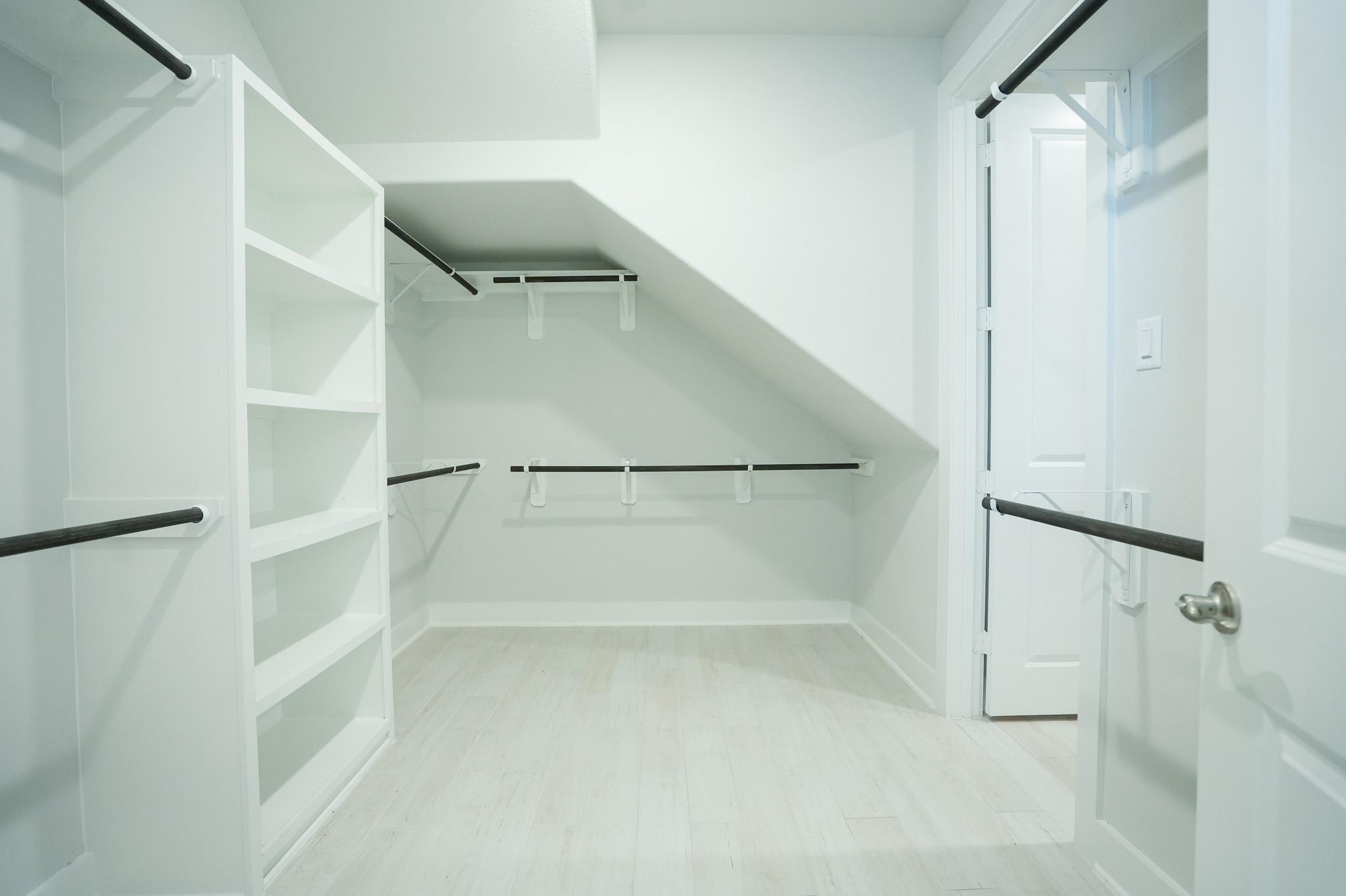 Spacious walk-in closet with white built-in shelving, hanging rods, and light wood flooring in Davidson Homes The Edward C, Lago Mar, Texas City