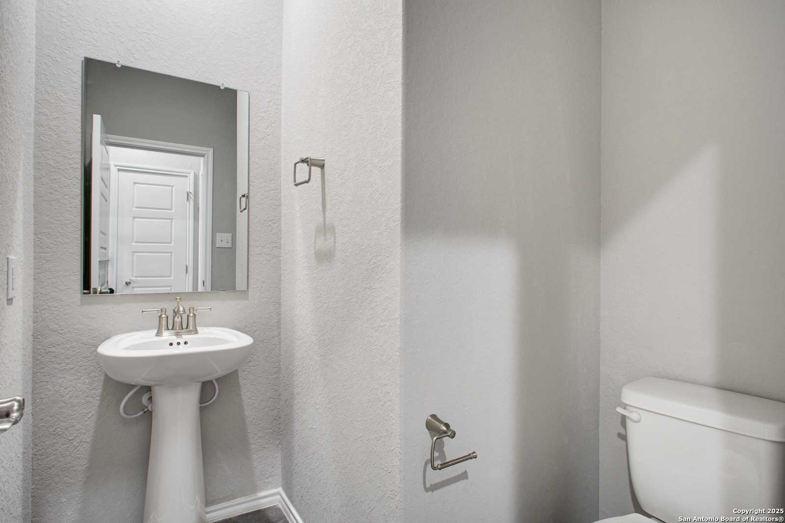 Modern powder room with white pedestal sink, frameless mirror, and toilet in Davidson Homes The Douglas G, San Antonio