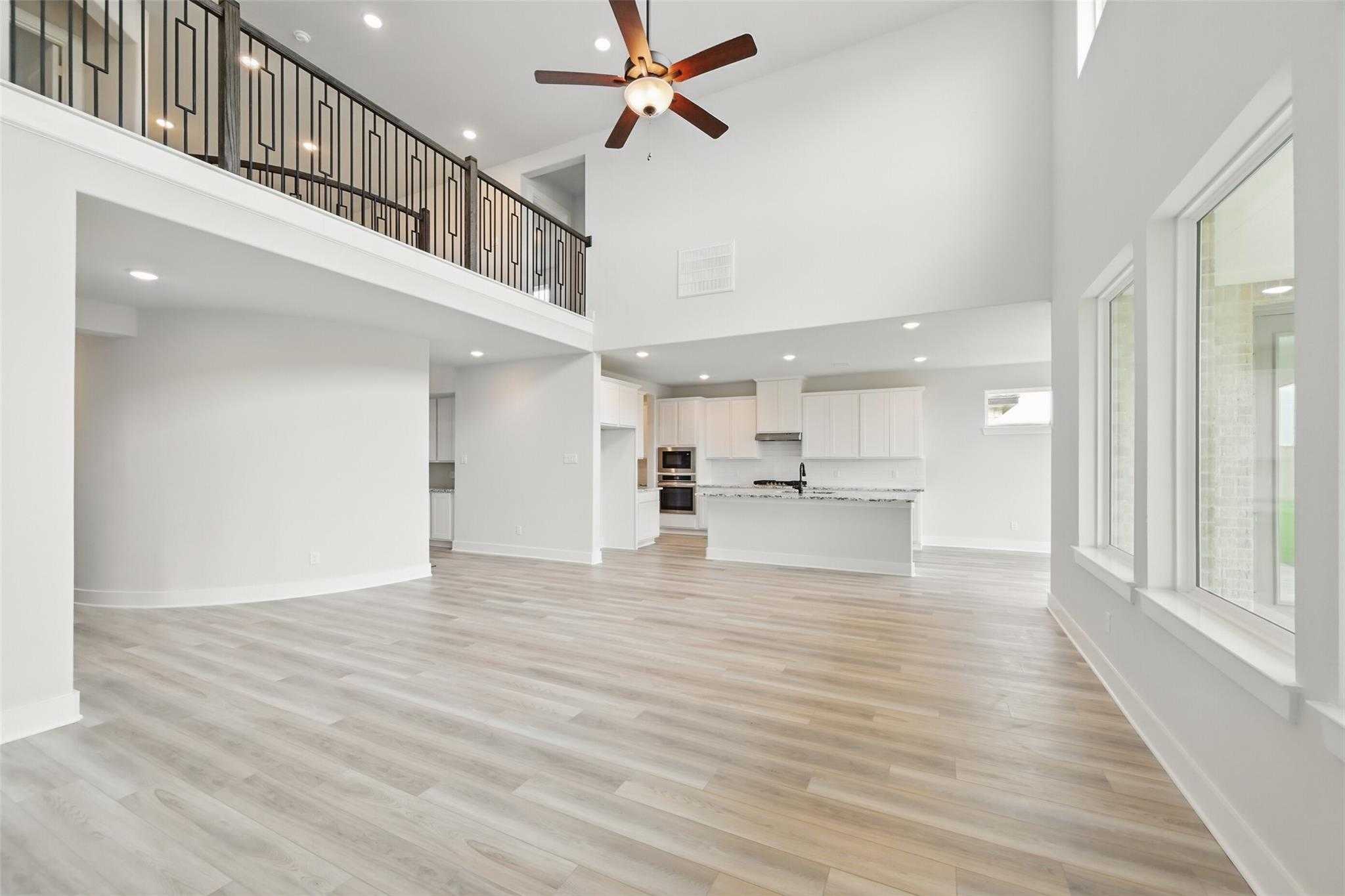 Spacious two-story great room with black metal balcony, ceiling fan, open white kitchen, and large windows in Davidson Homes The Victoria C, Lago Mar