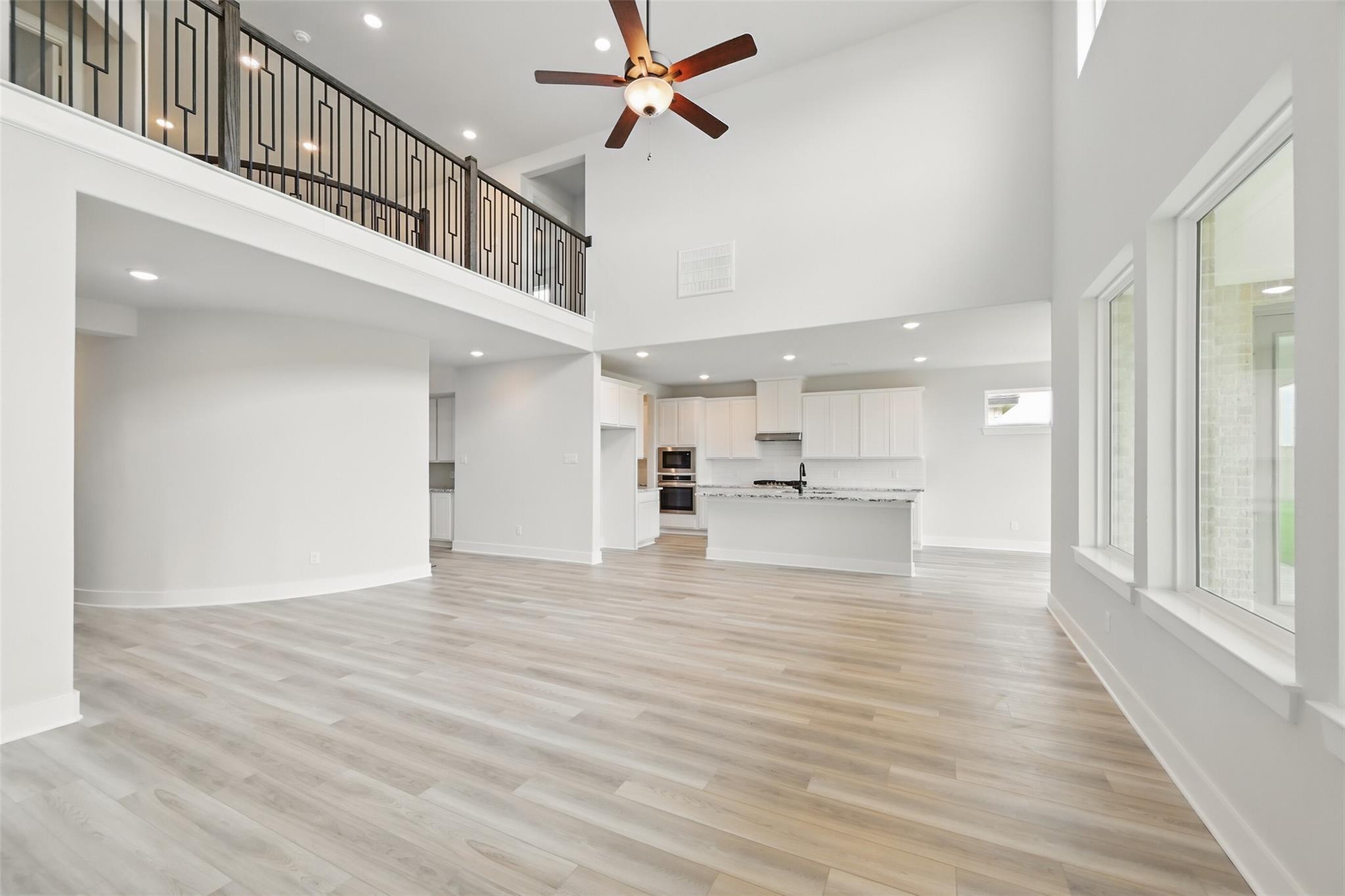 Spacious two-story great room with black metal balcony, ceiling fan, open white kitchen, and large windows in Davidson Homes The Victoria C, Lago Mar