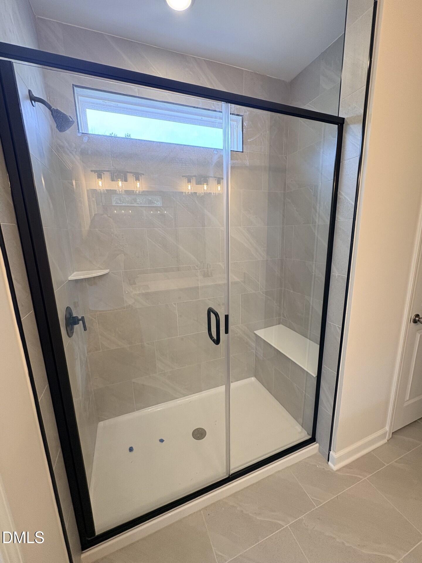 Modern walk-in tile shower with glass door and built-in bench in The Ash C floor plan at Woodland Crossing, Zebulon, NC.