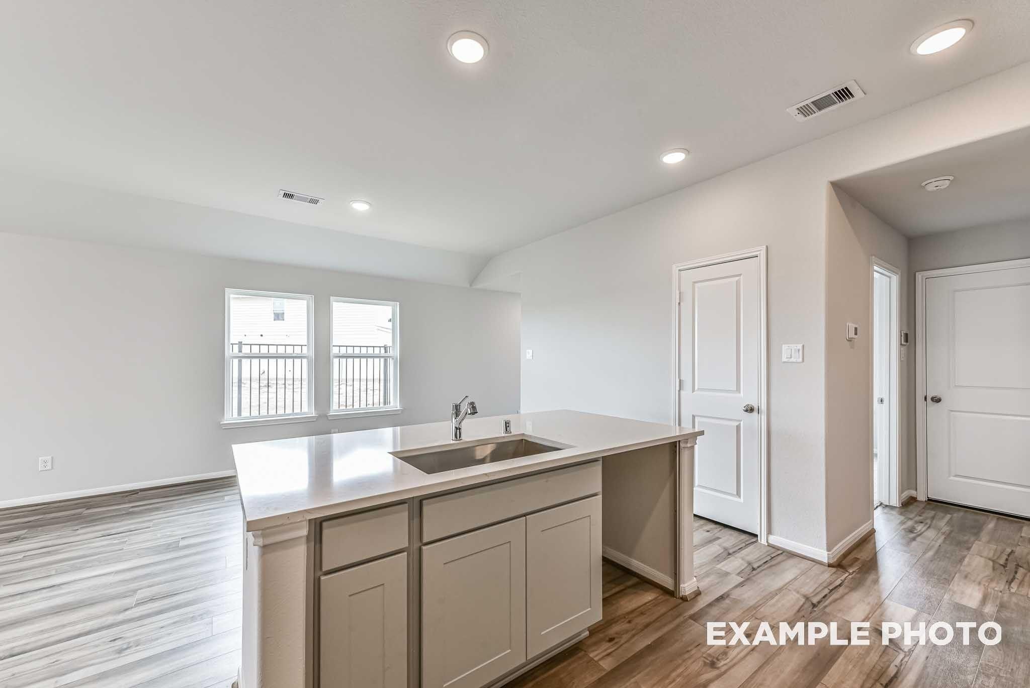 Bright kitchen island with white countertops and sink, wood-look flooring in The Costa A floor plan home in Dayton, Texas