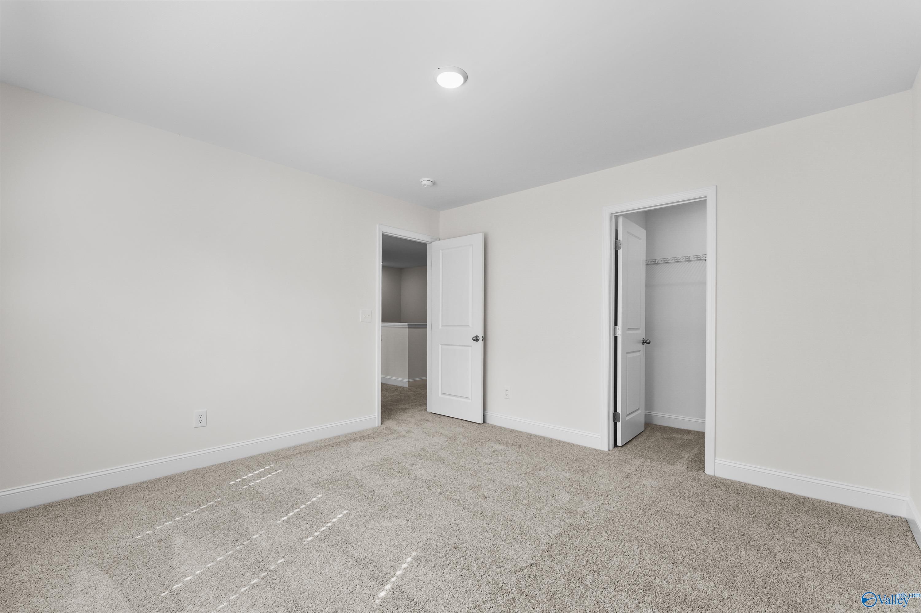 Spacious secondary bedroom with beige carpet, white walls, walk-in closet, and en-suite bath in Davidson Homes The Shelby A, Athens, Alabama