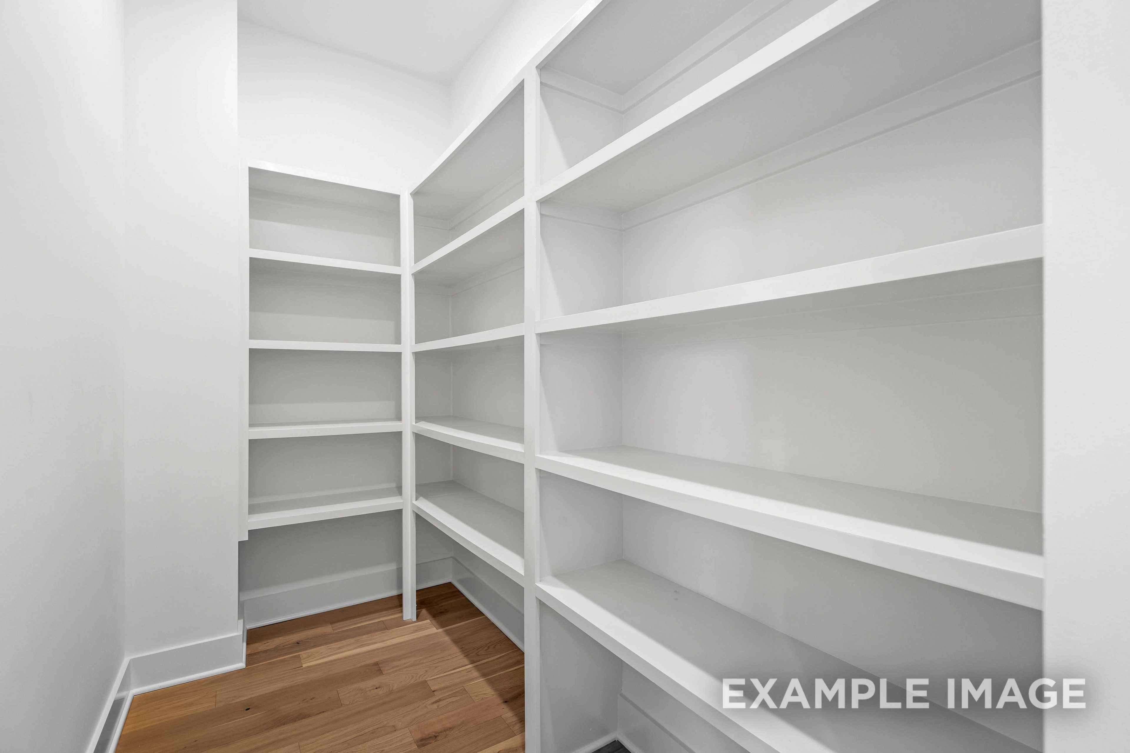 Spacious walk-in closet in The Albany A with white built-in shelving, hardwood floors, and bright white walls