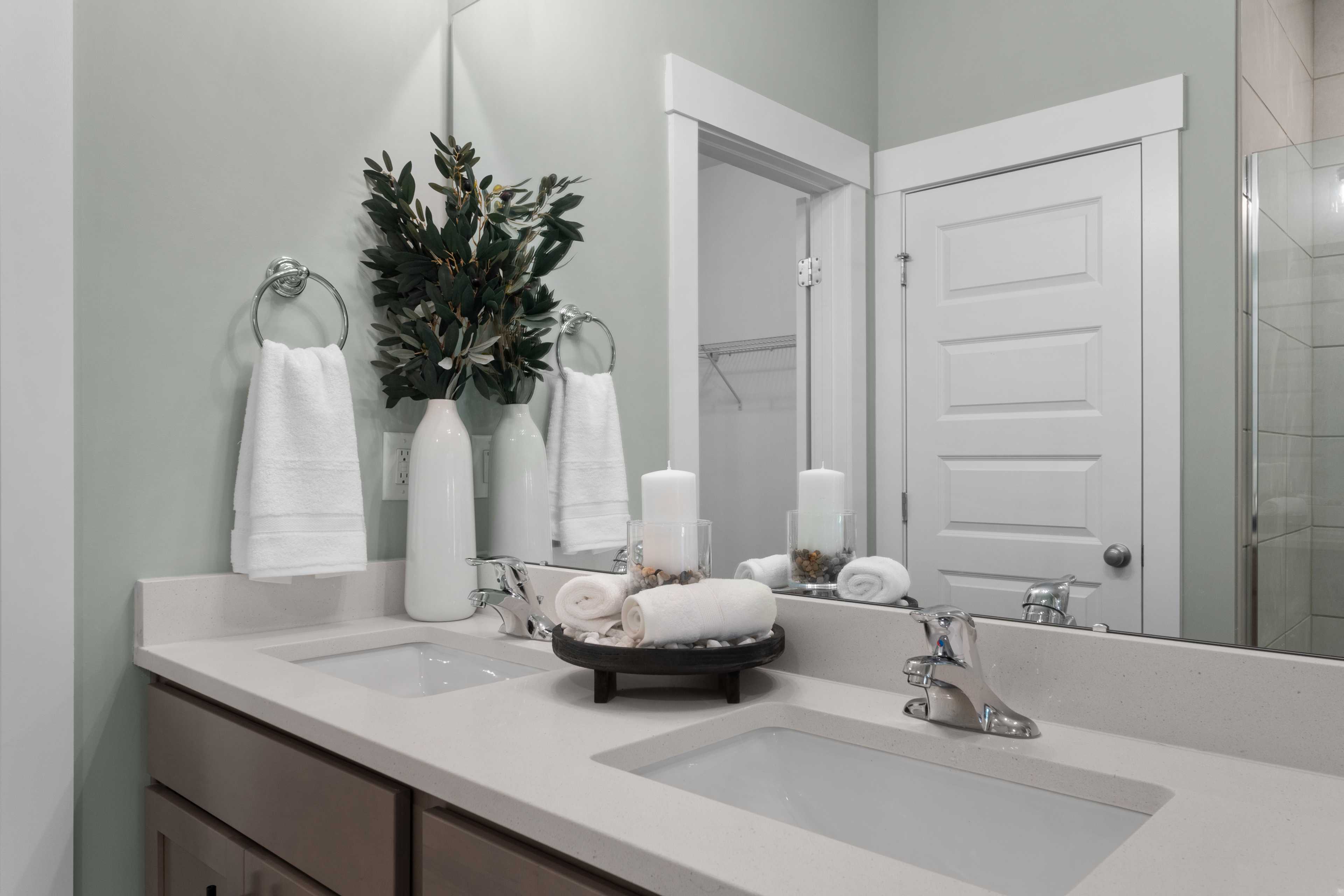 Spa-inspired bathroom vanity at Hollon Meadow in Decatur Alabama with double sinks, white quartz counters, rolled towels, and greenery accents