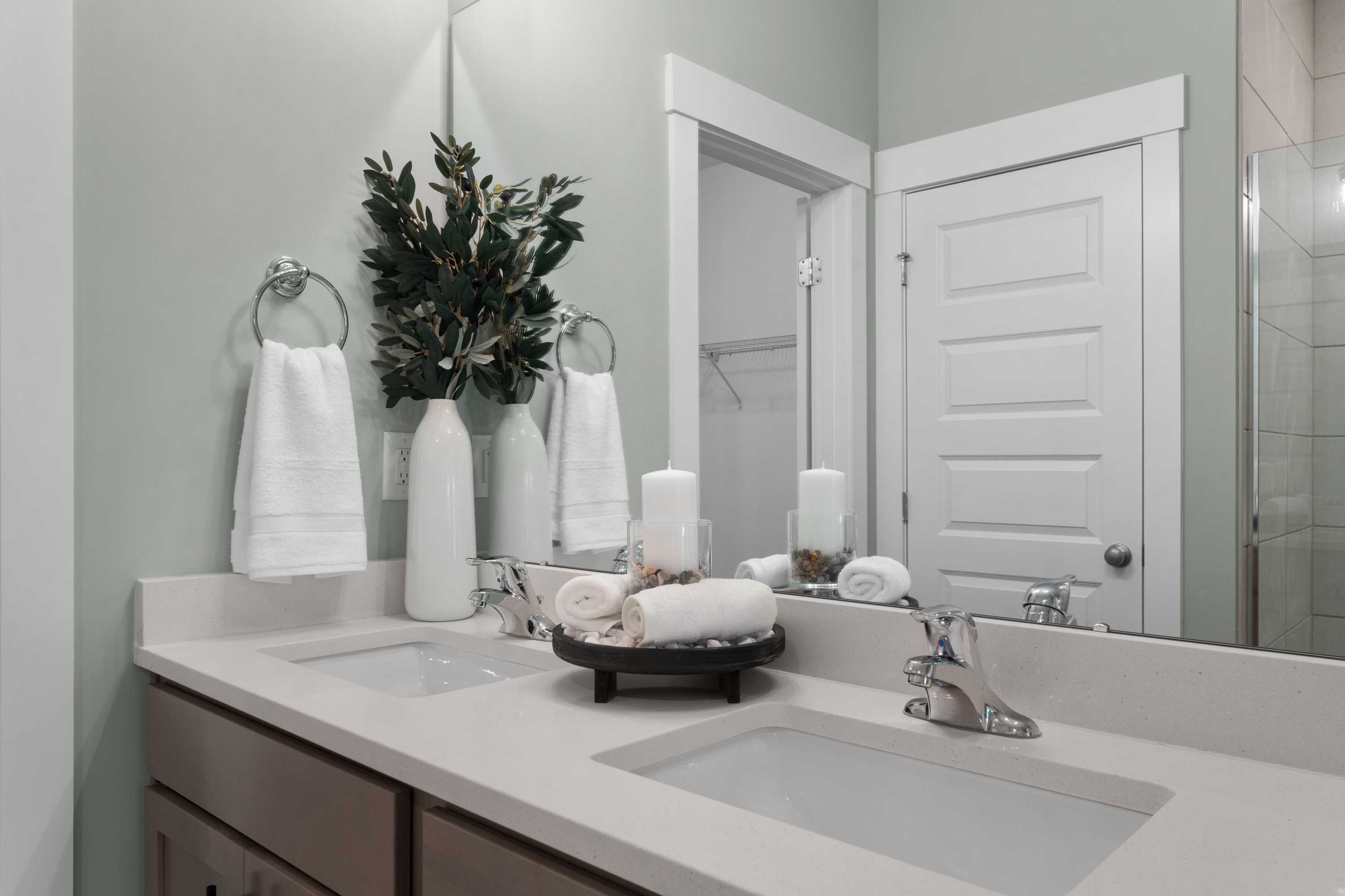 Spa-inspired bathroom vanity at Hollon Meadow in Decatur Alabama with double sinks, white quartz counters, rolled towels, and greenery accents