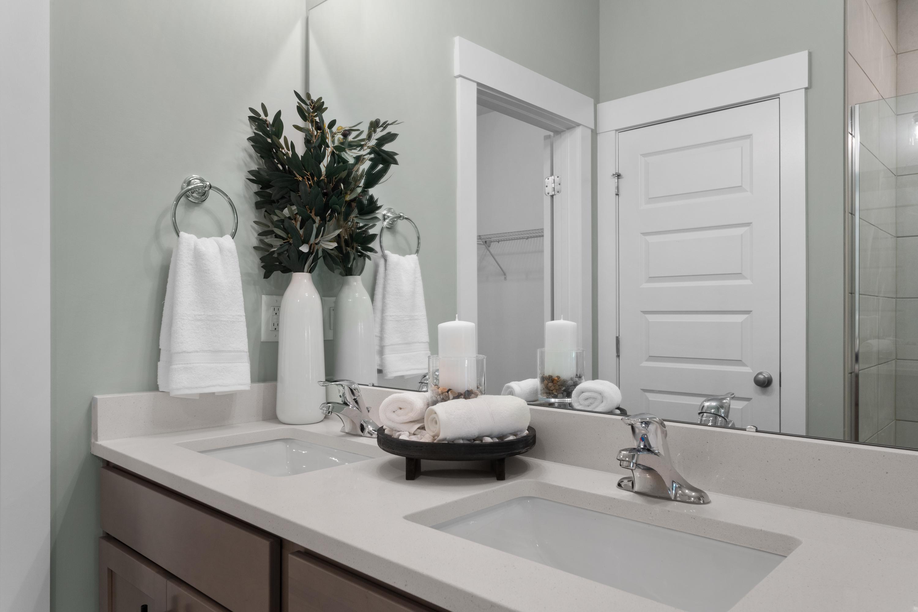 Spa-inspired bathroom vanity at Hollon Meadow in Decatur Alabama with double sinks, white quartz counters, rolled towels, and greenery accents