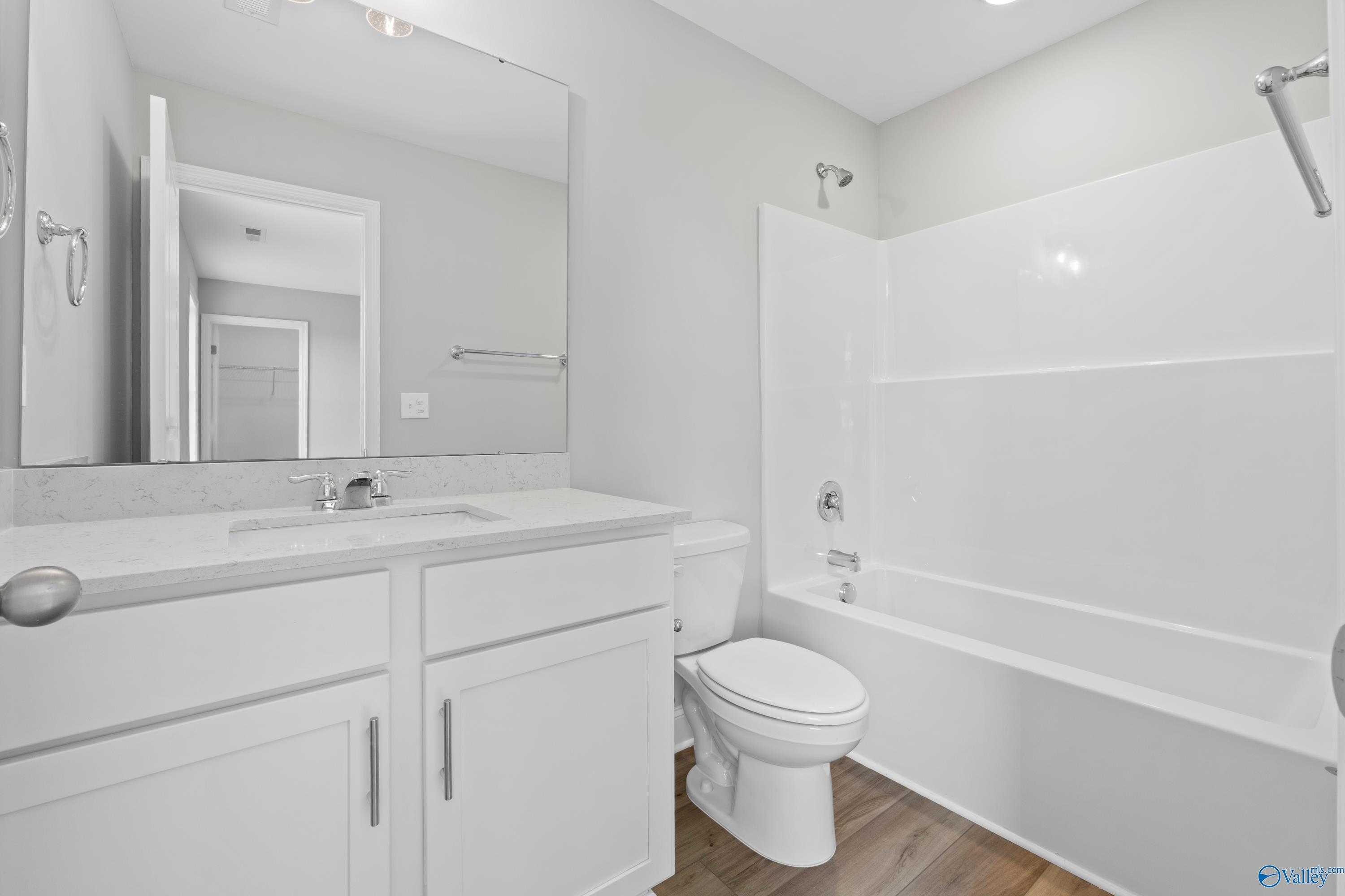 Modern bathroom with white double vanity, soaking tub, shower combo, and wood flooring in Davidson Homes The Chelsea B, New Market, Alabama