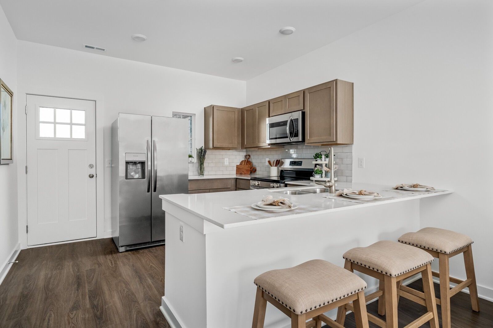 Bright kitchen with white island, beige cabinets, stainless fridge, and bar stools in The Cumberland A, Davidson Homes, Gallatin, TN