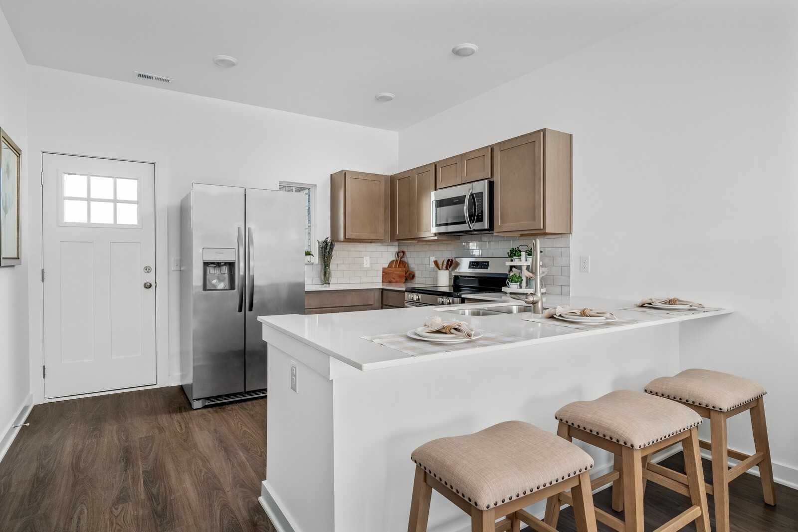 Bright kitchen with white island, beige cabinets, stainless fridge, and bar stools in The Cumberland A, Davidson Homes, Gallatin, TN