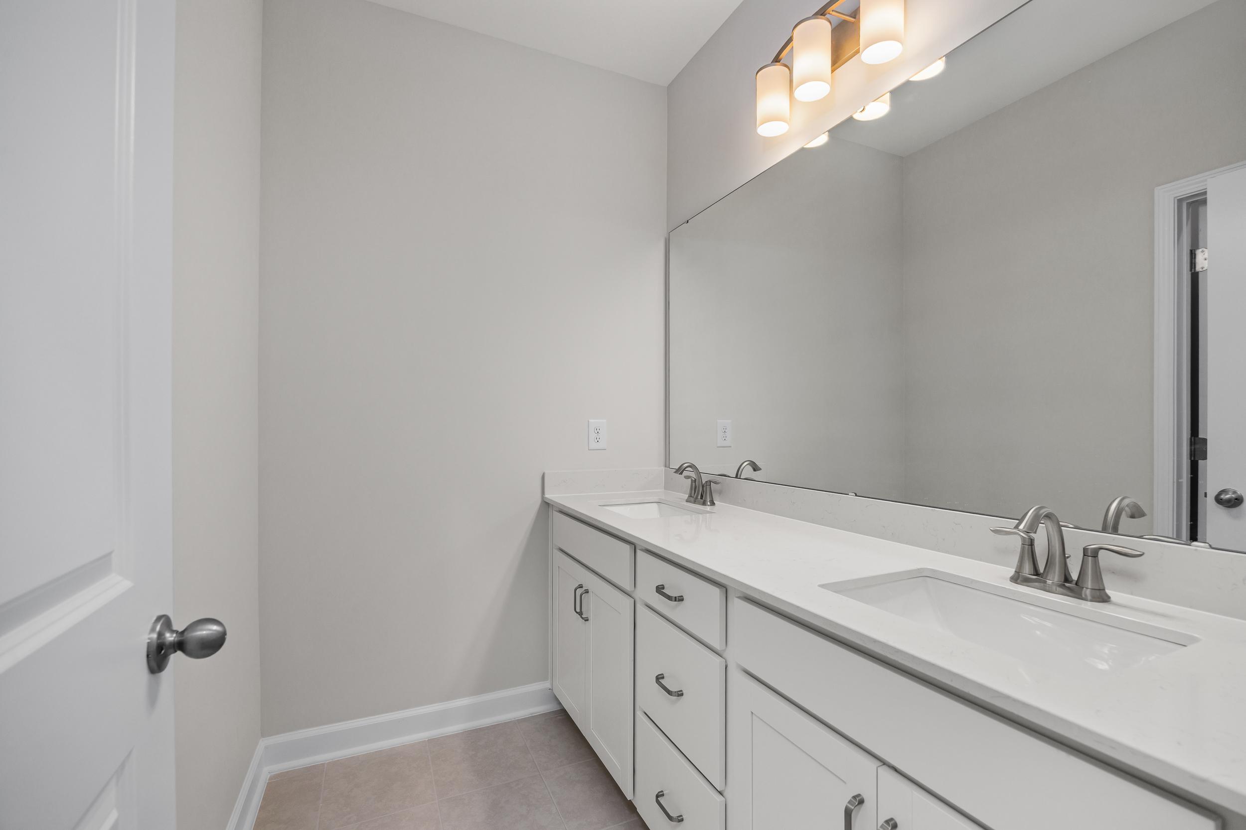 Modern master bathroom in The Aspen by Davidson Homes with white double vanity, large mirror, and gray walls