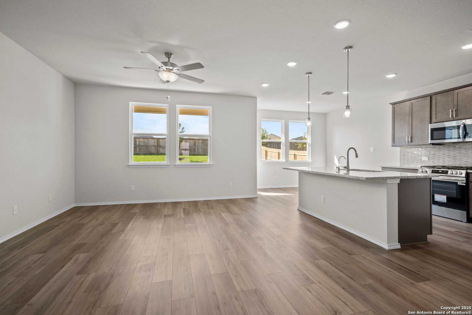 Open-concept kitchen and living area with wood floors, ceiling fan, large windows, and stainless appliances in Davidson Homes The Asheville J, San Antonio