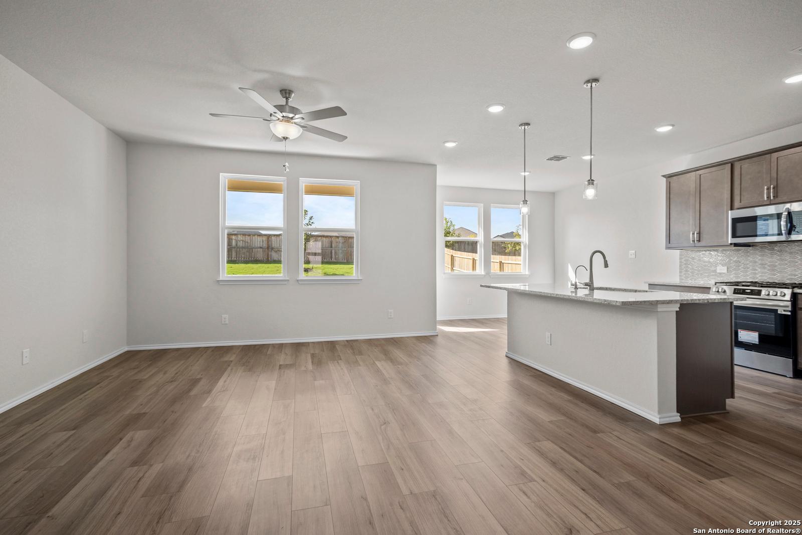 Open-concept kitchen and living area with wood floors, ceiling fan, large windows, and stainless appliances in Davidson Homes The Asheville J, San Antonio