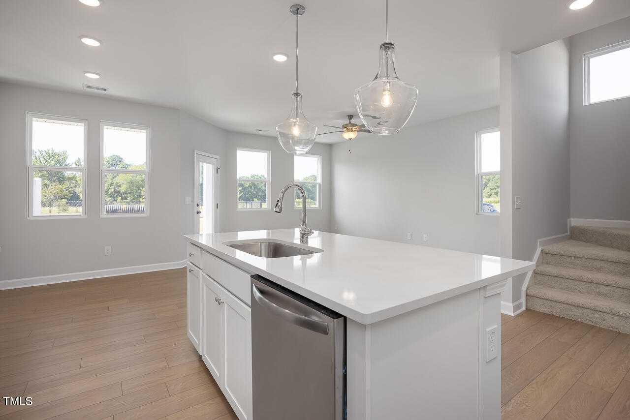 Bright modern kitchen with white quartz island, stainless dishwasher, pendant lights, and large windows in Davidson Homes The Graham, Fuquay-Varina