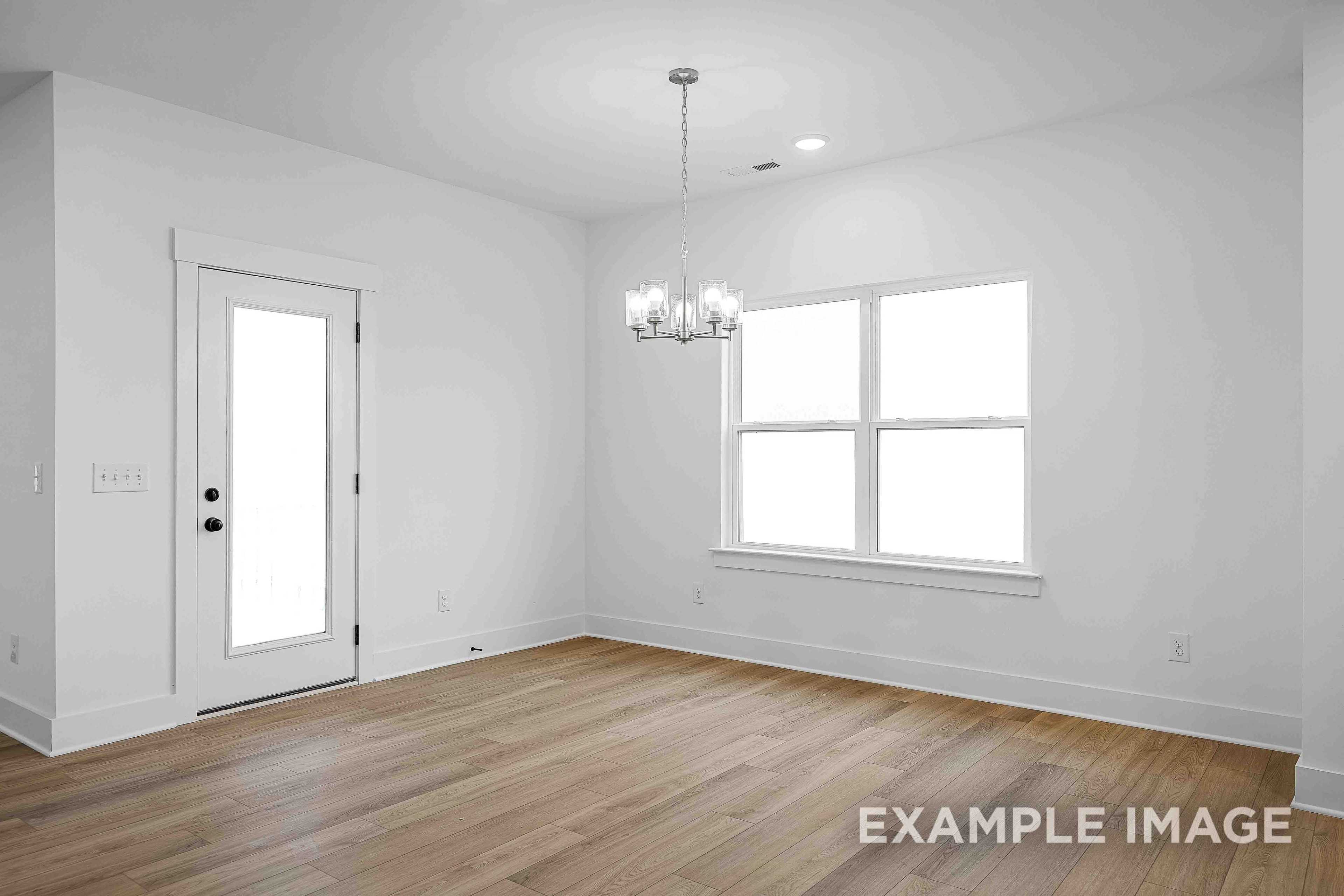 Spacious dining room in The Charleston with chandelier, large windows, white walls, and hardwood floors