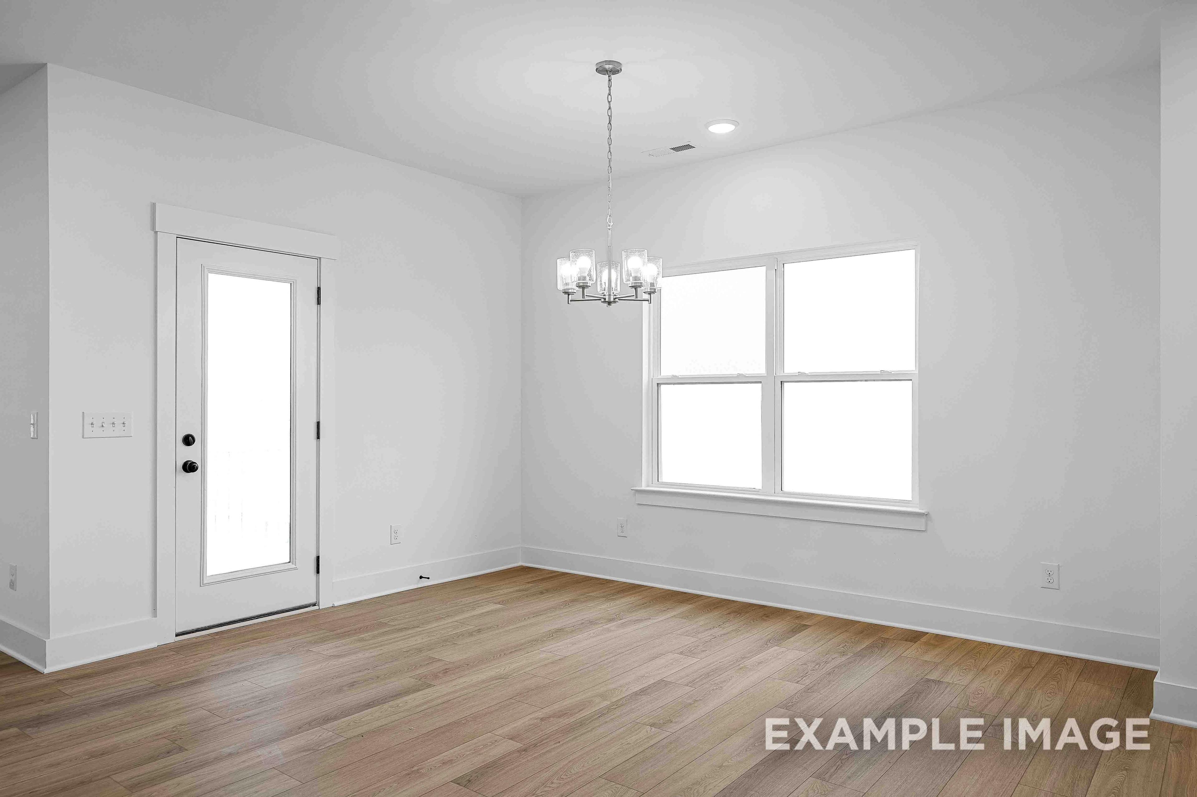 Spacious dining room in The Charleston with chandelier, large windows, white walls, and hardwood floors