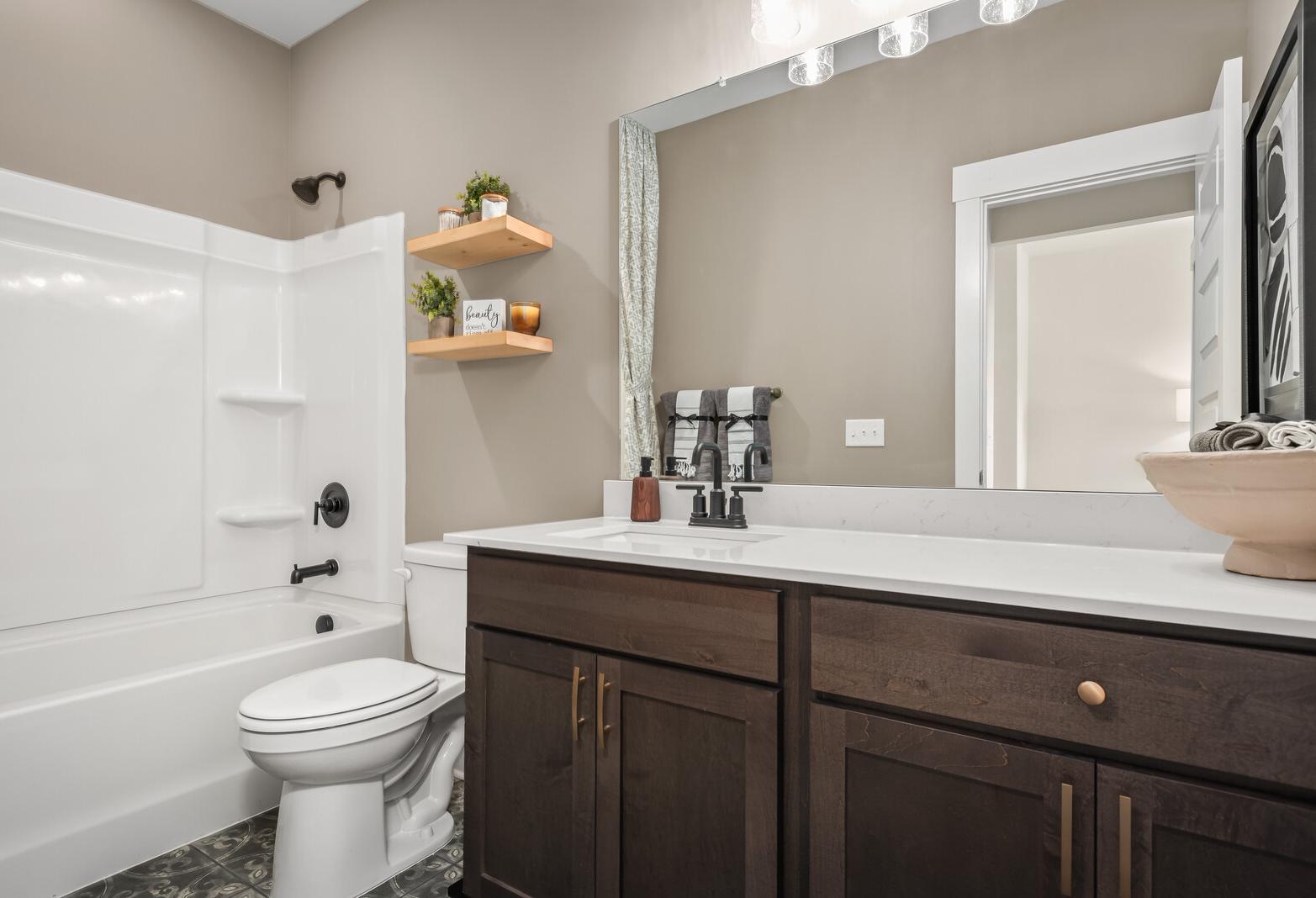 Spacious Ridgeport E master bathroom with white tub-shower combo, double shaker vanity, beige walls, and modern lighting by Davidson Homes