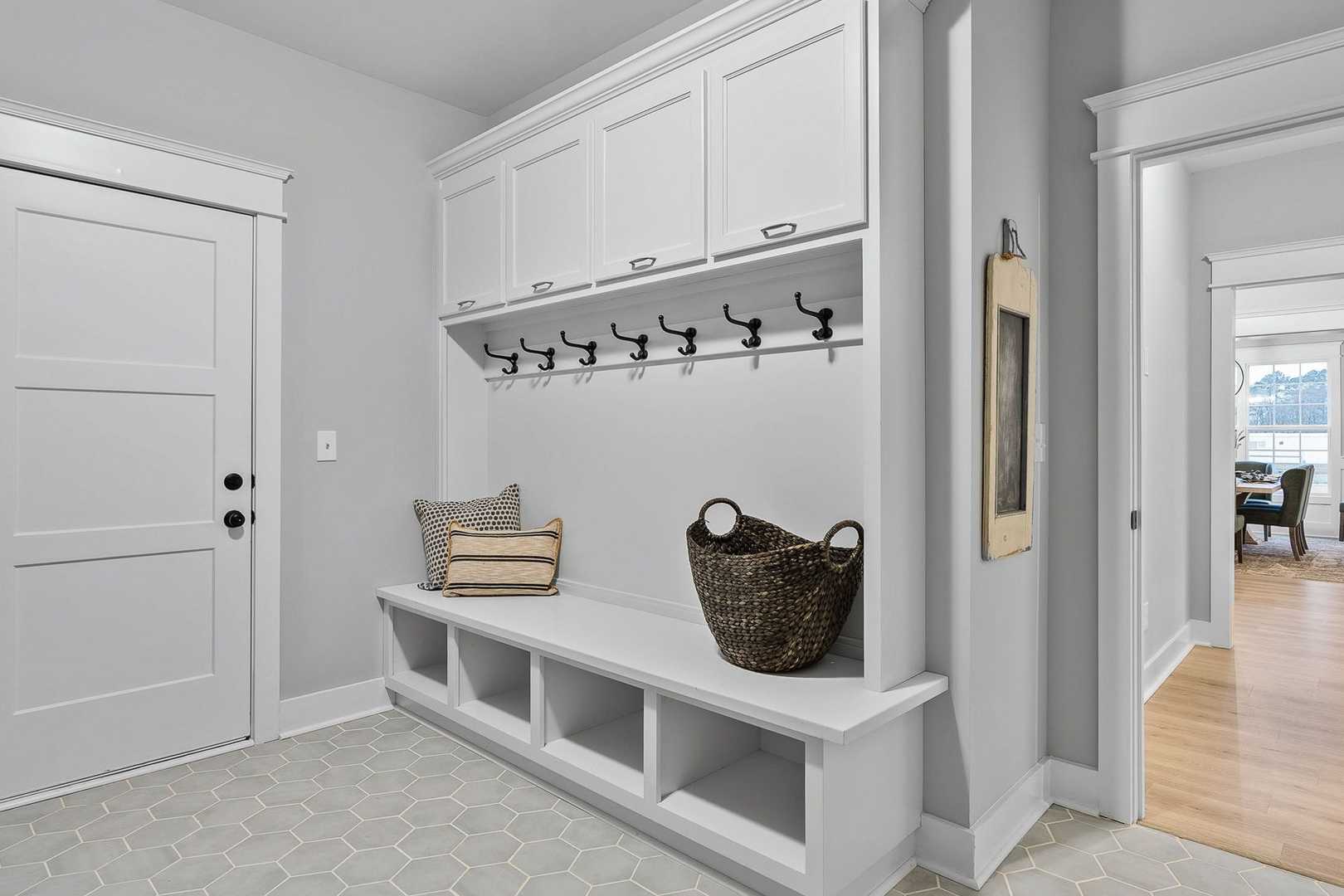 Spacious mudroom in The Oxford home design with white lockers, coat hooks, cushioned bench, and woven baskets