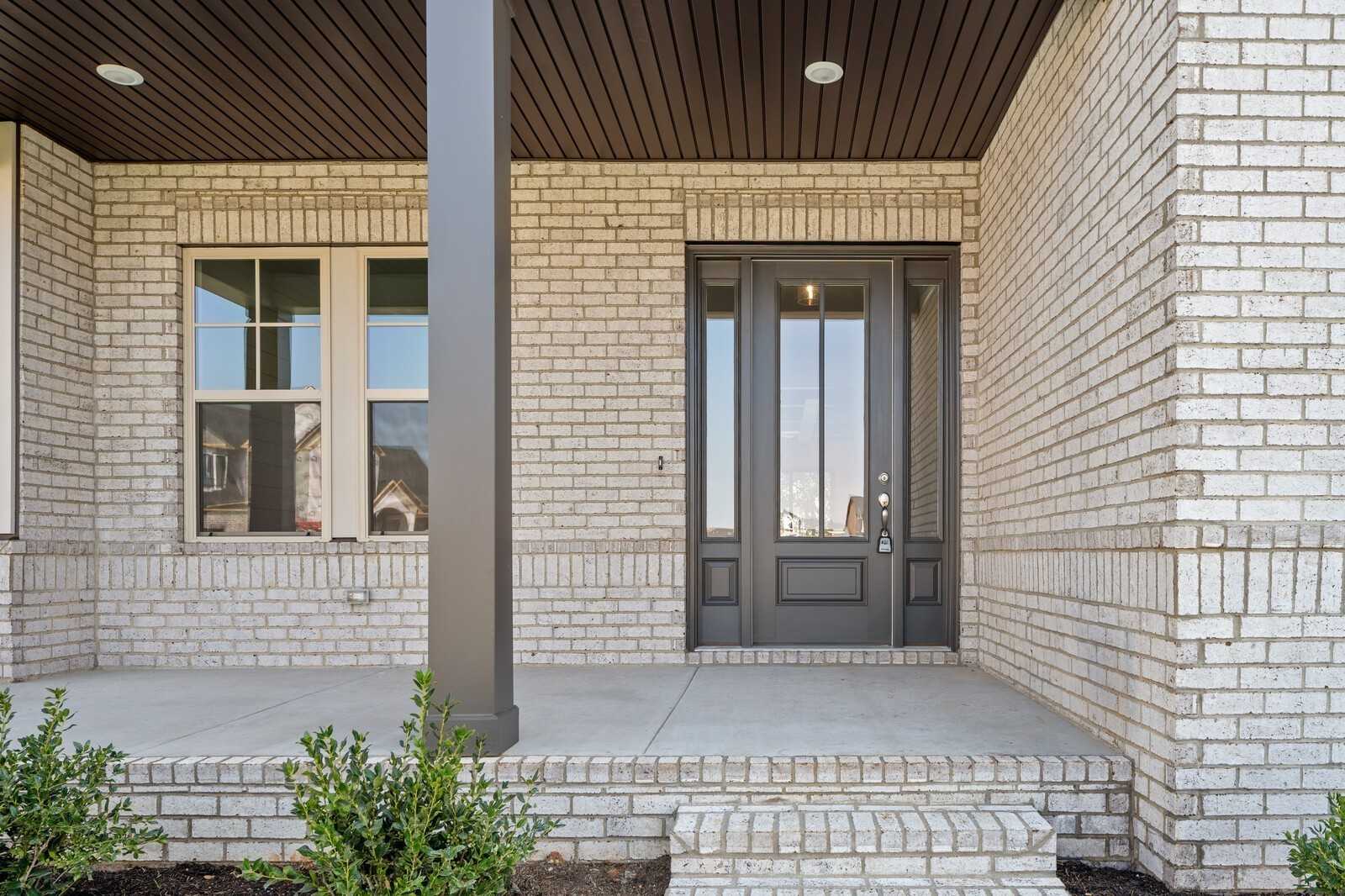 Elegant brick home front entrance with covered wooden porch, gray glass double doors, and sidelights in Davidson Homes The Albany A, Murfreesboro, Tennessee