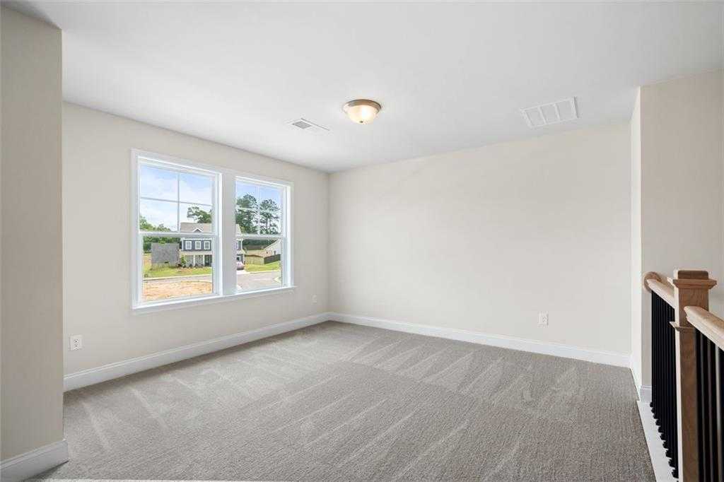 Spacious upstairs bedroom with large windows, beige walls, and balcony railing in Davidson Homes The Willow D at Wehunt Meadows, Hoschton, Georgia