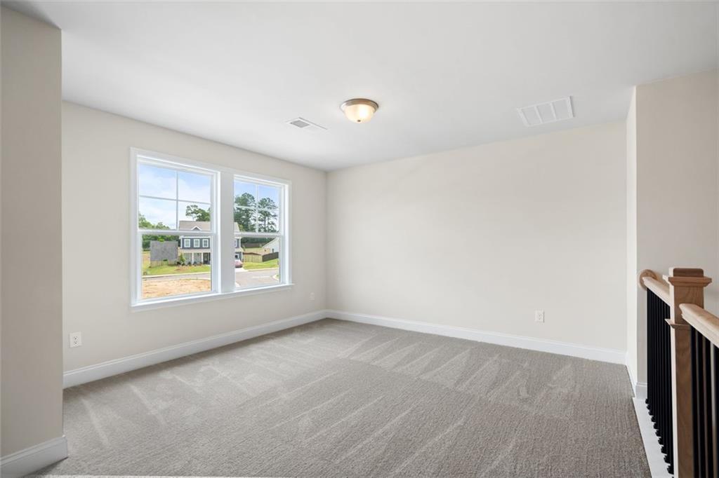 Spacious upstairs bedroom with large windows, beige walls, and balcony railing in Davidson Homes The Willow D at Wehunt Meadows, Hoschton, Georgia