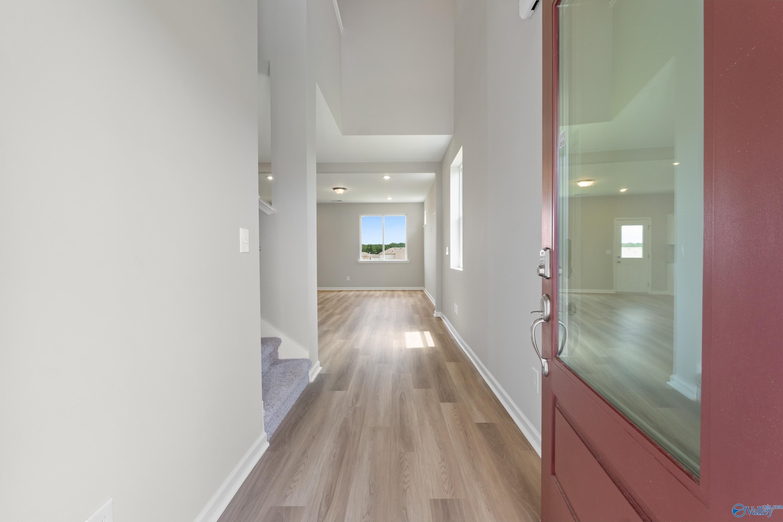 Bright two-story entry hallway with light hardwood floors, staircase, and red glass door in The Augusta floor plan, Madison, Alabama