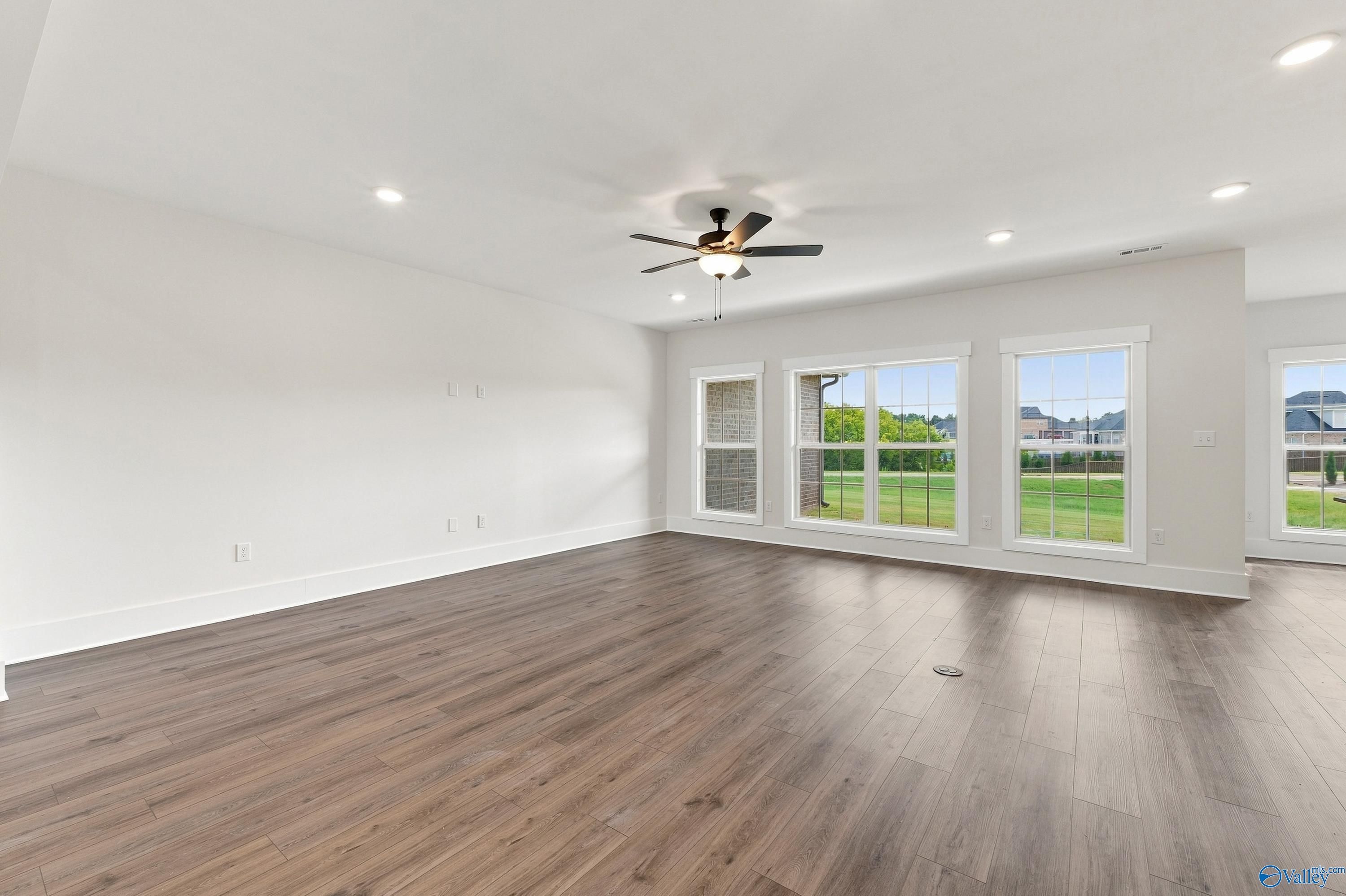 Bright open-concept great room with luxury vinyl plank flooring, ceiling fan, and large windows in Davidson Homes' Valencia floor plan, Huntsville