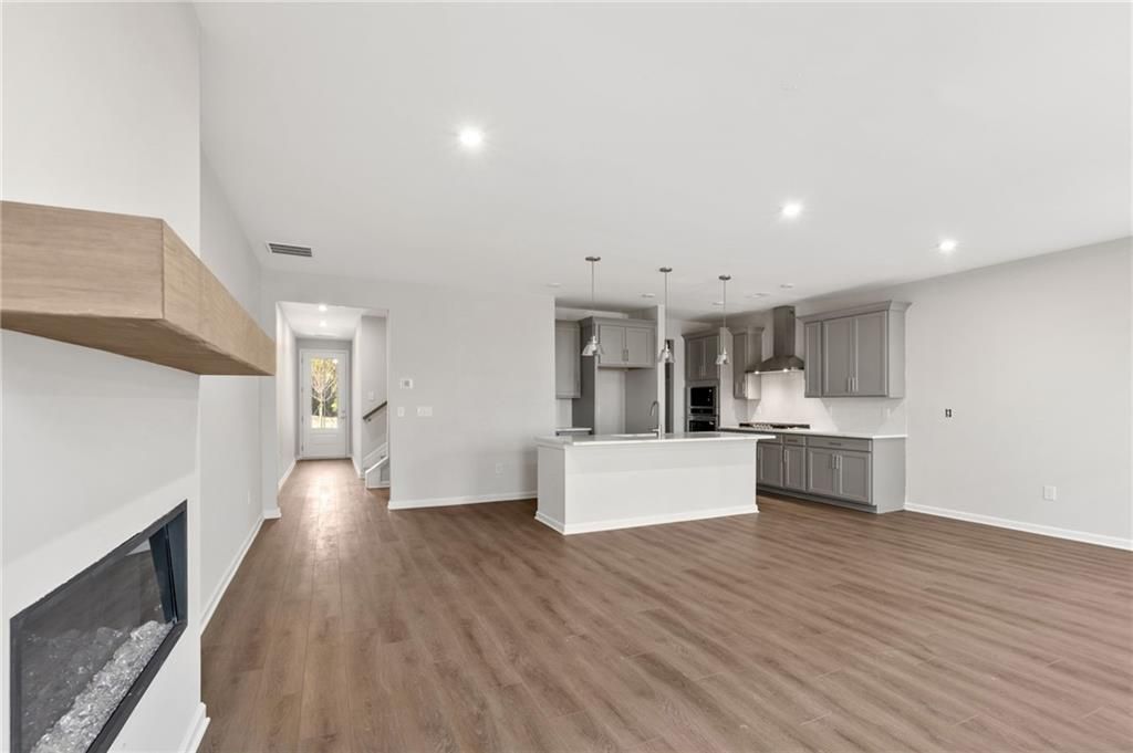Modern open-concept living room with gas fireplace and adjacent kitchen featuring white island cabinets in Davidson Homes The Marion A, Winder, Georgia