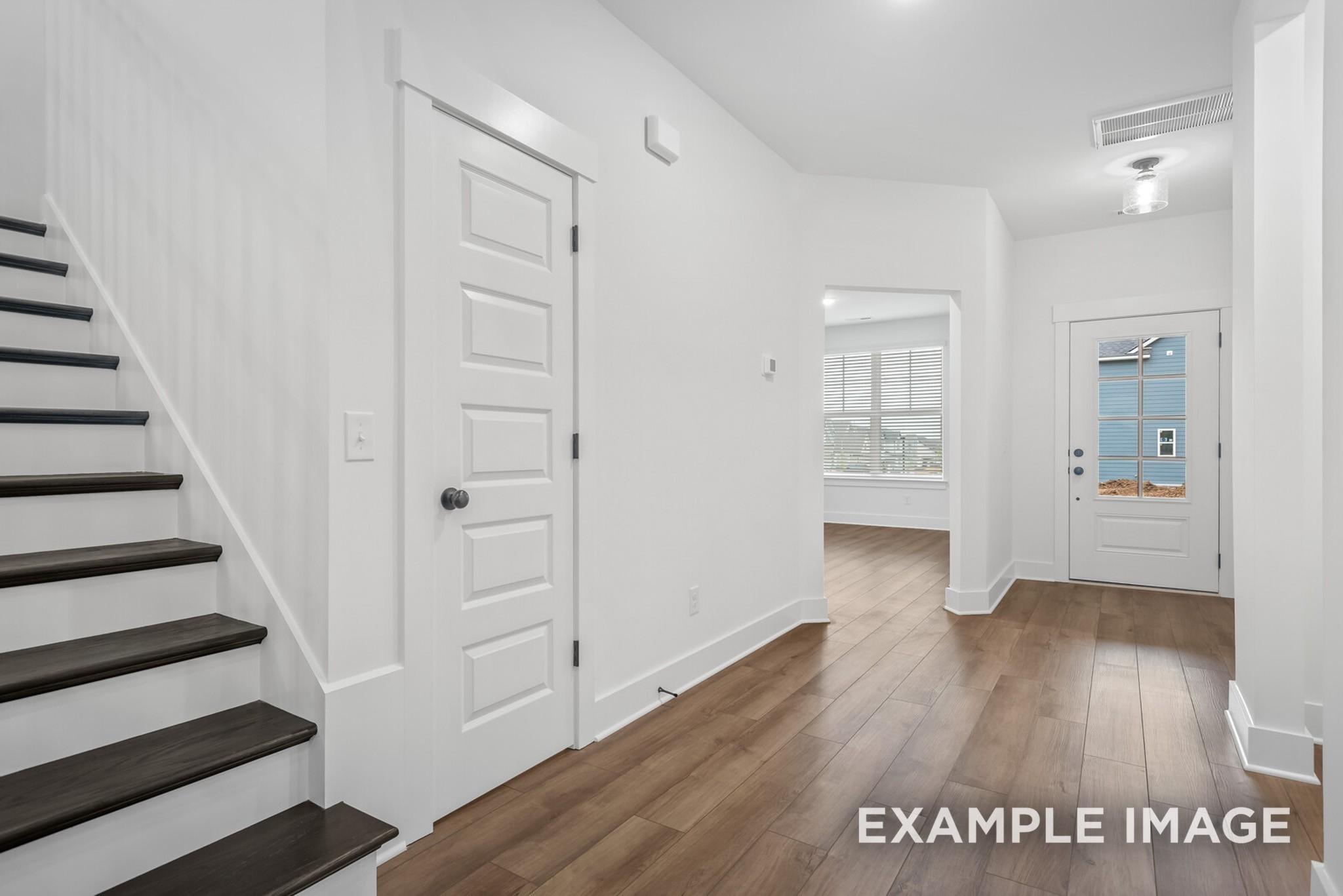 Bright entry foyer with dark wood staircase, white paneled doors, and hardwood floors in Davidson Homes Ridgeport C, Gallatin, TN