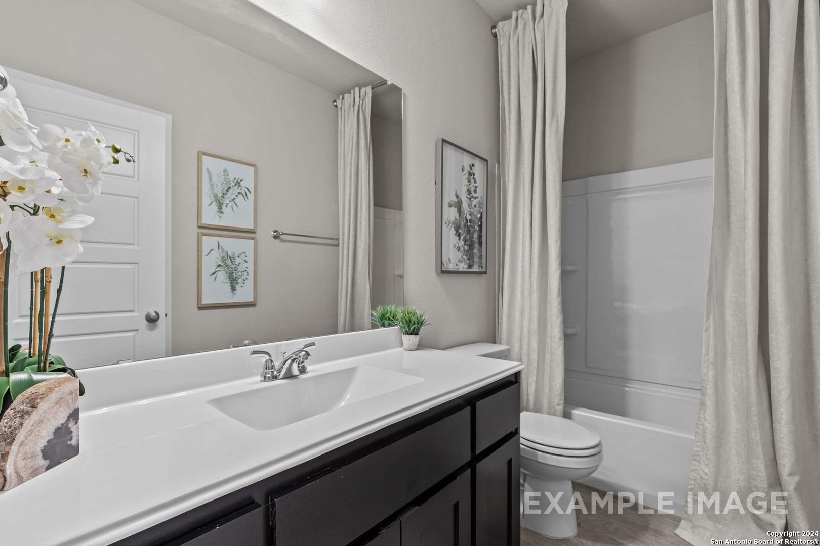Elegant primary bathroom with white quartz vanity, dark cabinets, soaking tub, orchids, and framed art in Davidson Homes The Collin A, Seguin, TX