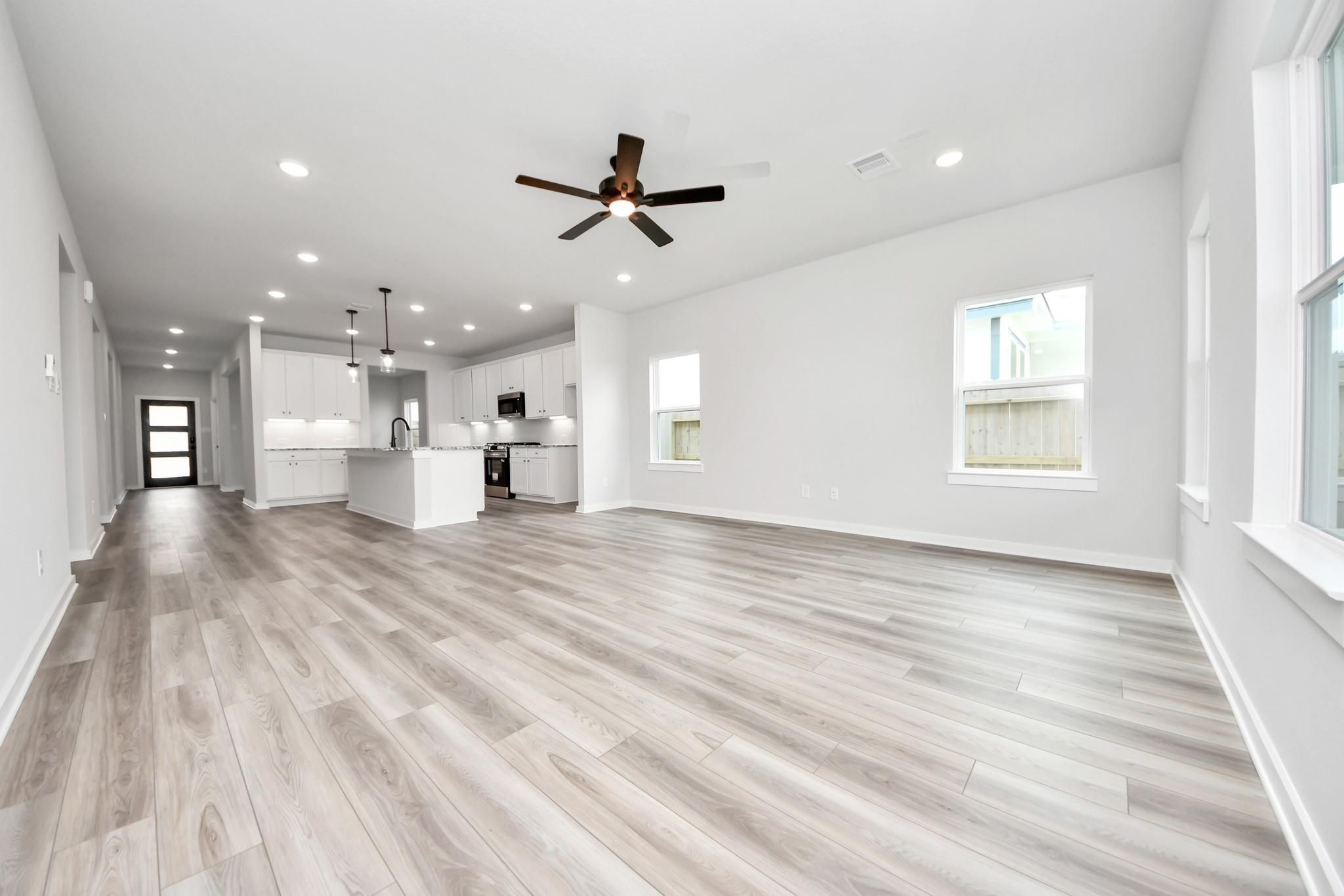 Open-concept living room and kitchen with wood-look flooring in The Sorrento E floor plan at Sundance Cove, Crosby, Texas.