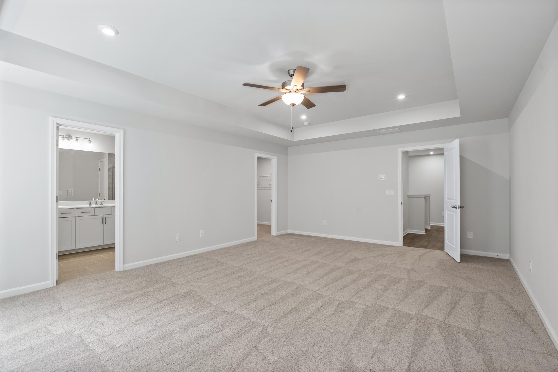 Spacious master bedroom in The Cary A featuring ceiling fan, en-suite bath with vanity, and walk-in closet