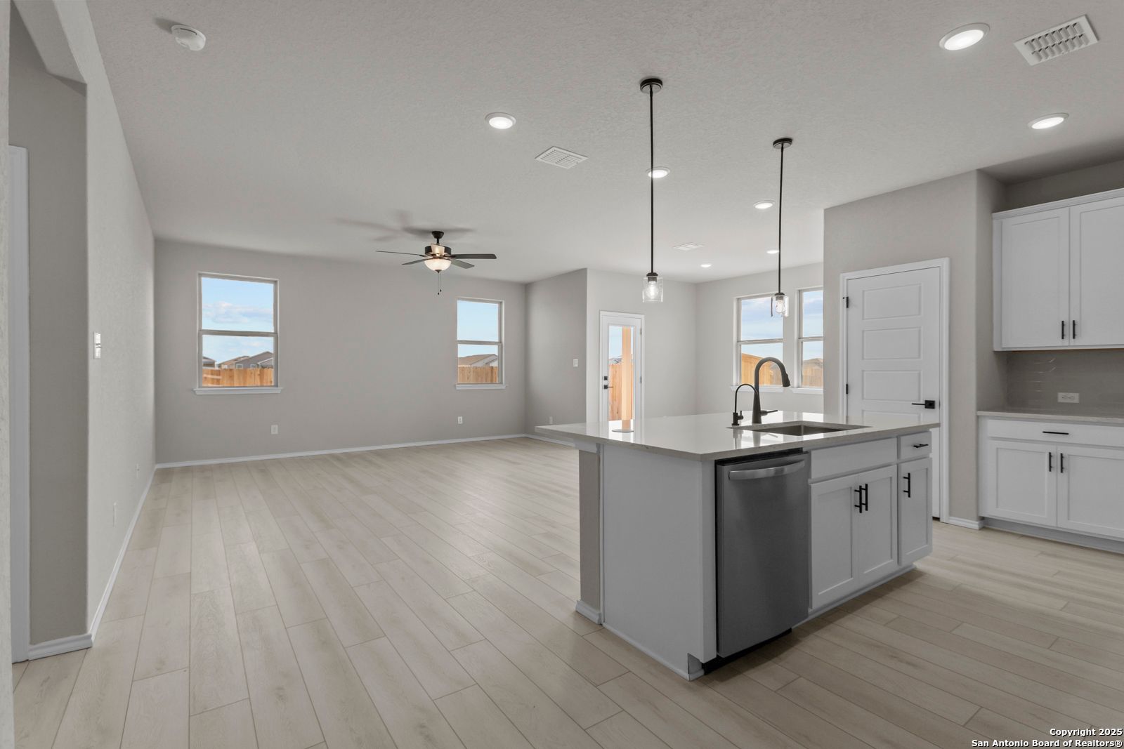 Modern open-concept kitchen with gray island, white cabinets, pendant lights, and wood flooring in Davidson Homes The Daphne H, Seguin, Texas