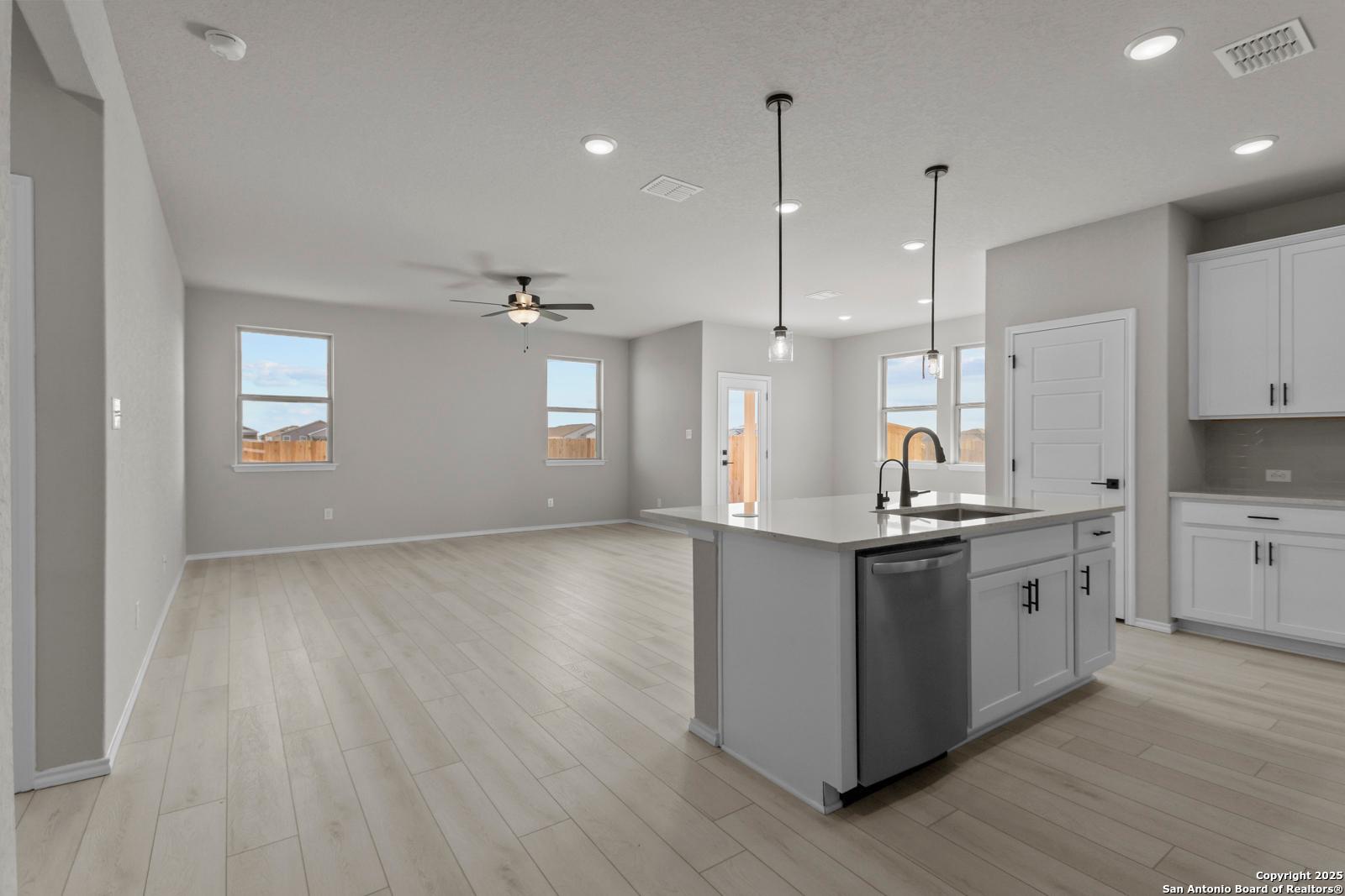 Modern open-concept kitchen with gray island, white cabinets, pendant lights, and wood flooring in Davidson Homes The Daphne H, Seguin, Texas